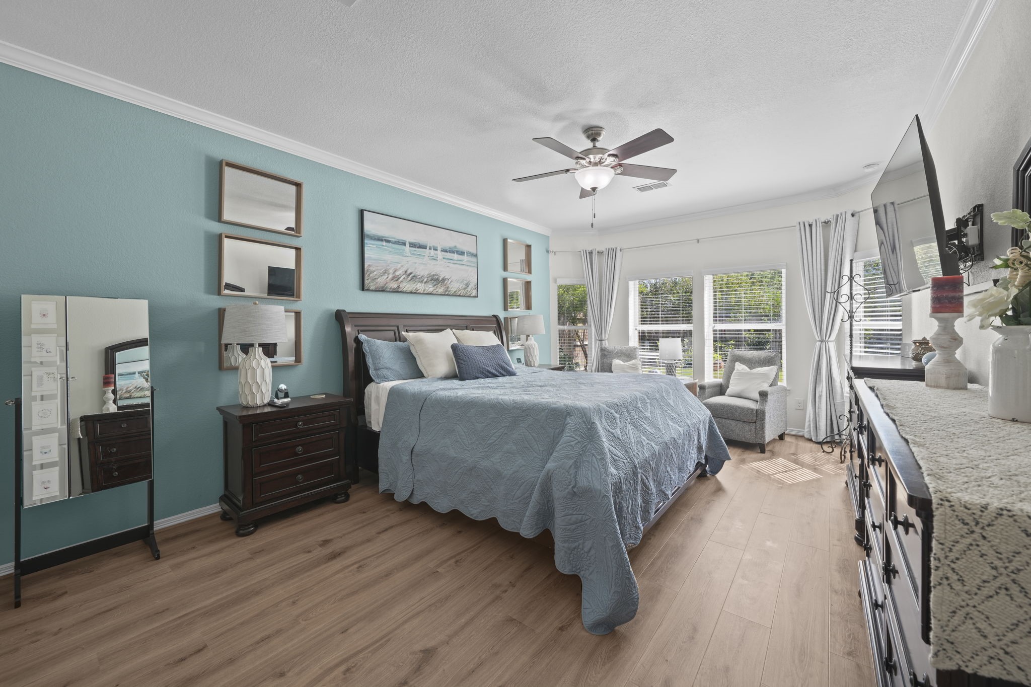 Spacious and bright bedroom featuring a cozy sitting area by large windows, elegant wood flooring, and stylish decor with a calming color palette.