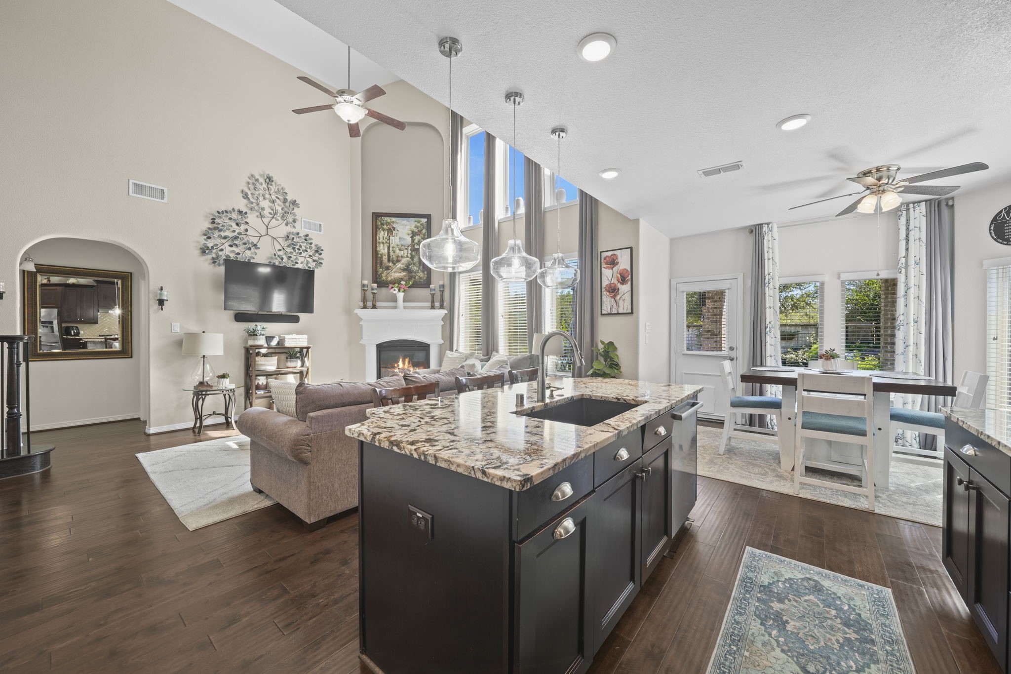 Experience open-concept living with this elegant space featuring a gourmet kitchen with granite countertops and a large island, leading to a cozy living area with high ceilings and a fireplace. Natural light floods through expansive windows, illuminating the dining area with garden views.
