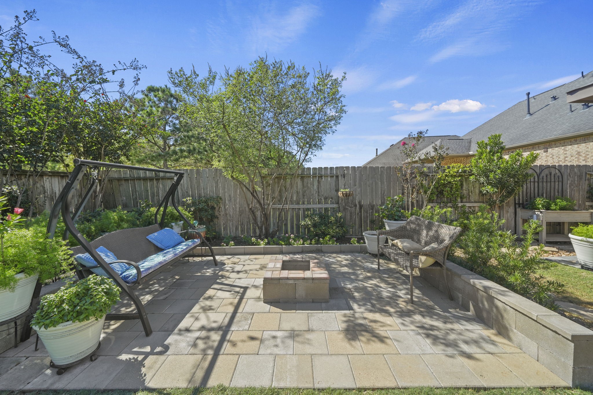 Charming backyard retreat featuring a cozy swing, lush greenery, and a central fire pit for outdoor relaxation and entertaining.