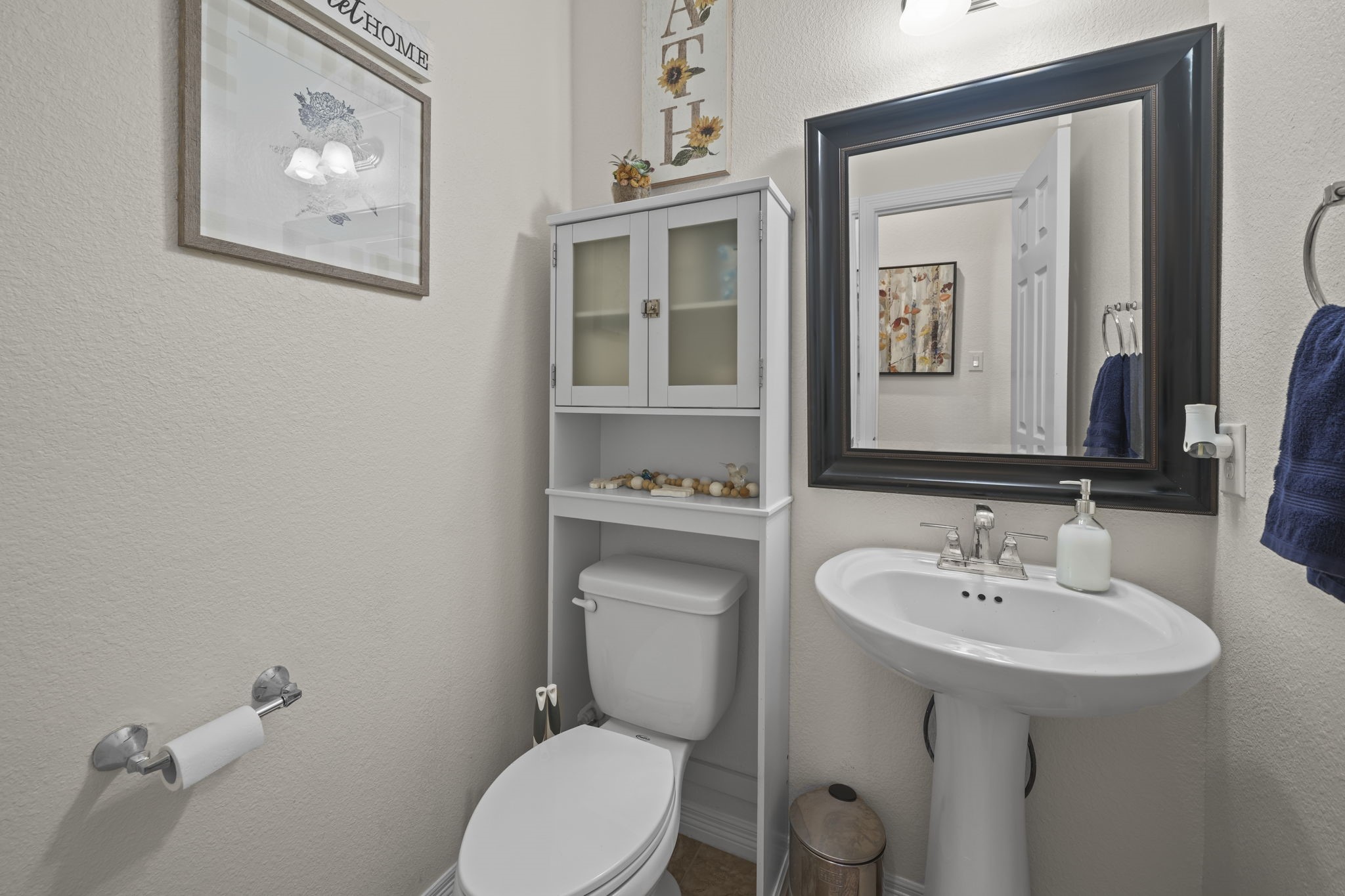 Charming and efficient powder room featuring a sleek pedestal sink, elegant wall mirror, and convenient storage above the toilet.