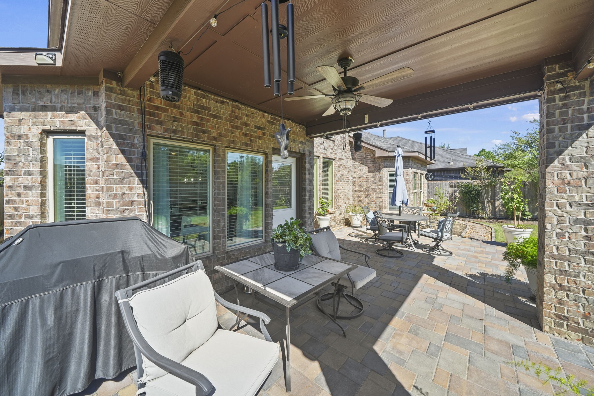 Charming brick patio featuring a covered seating area with a ceiling fan, perfect for outdoor dining and relaxation, complete with a barbecue grill and elegant landscaping.