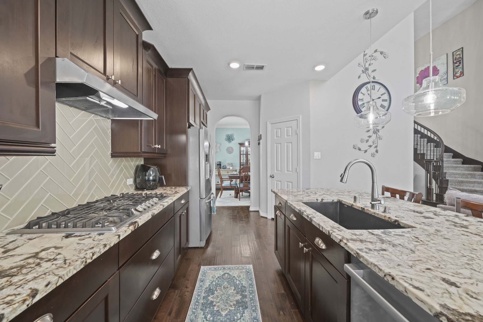 Elegant kitchen featuring rich dark wood cabinetry, granite countertops, and a stylish backsplash. The space is enhanced by modern pendant lighting and a spacious island with a built-in sink, perfect for entertaining.
