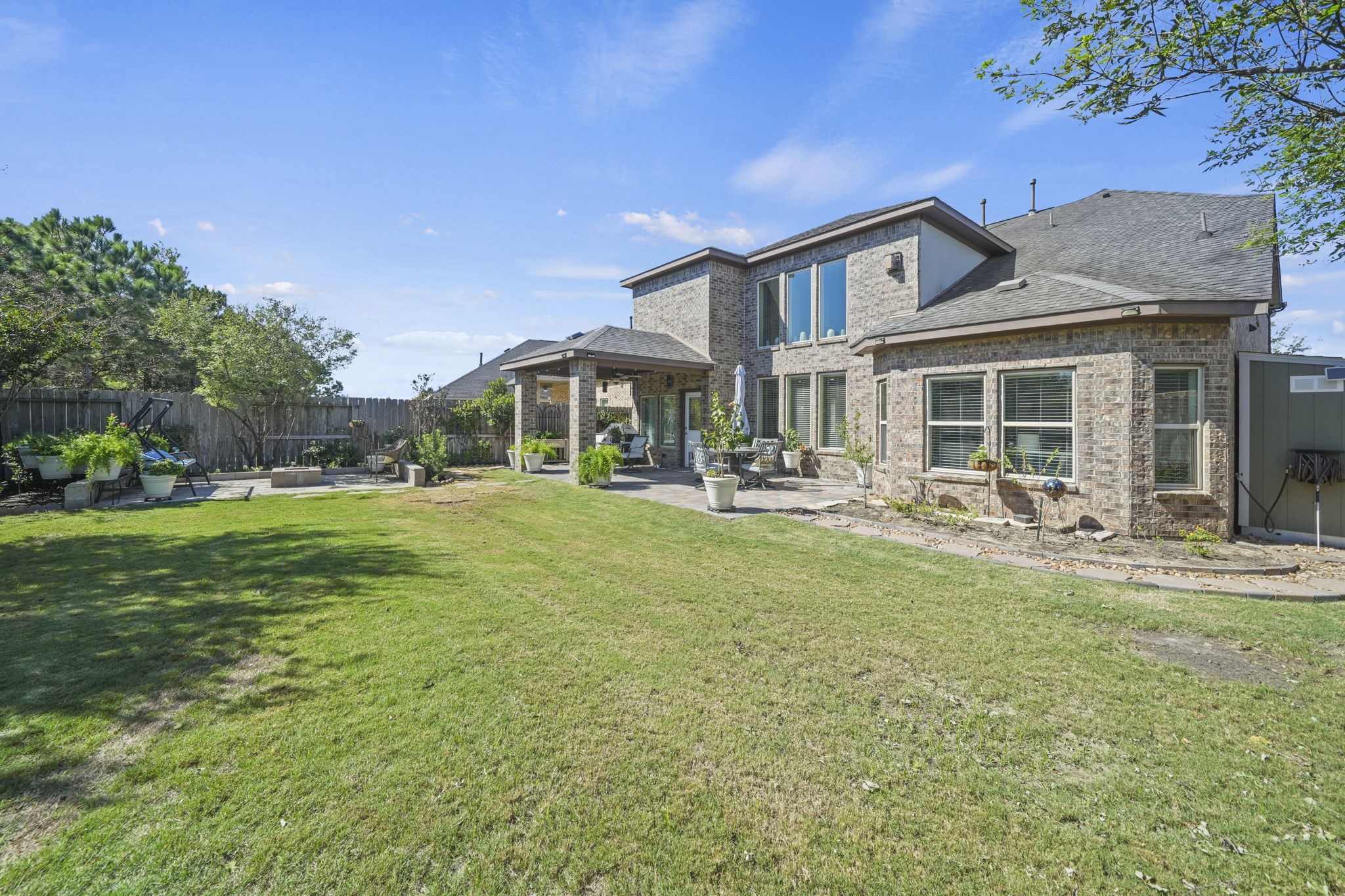 Spacious backyard with lush green lawn and a charming brick exterior, complemented by a covered patio perfect for outdoor entertaining.