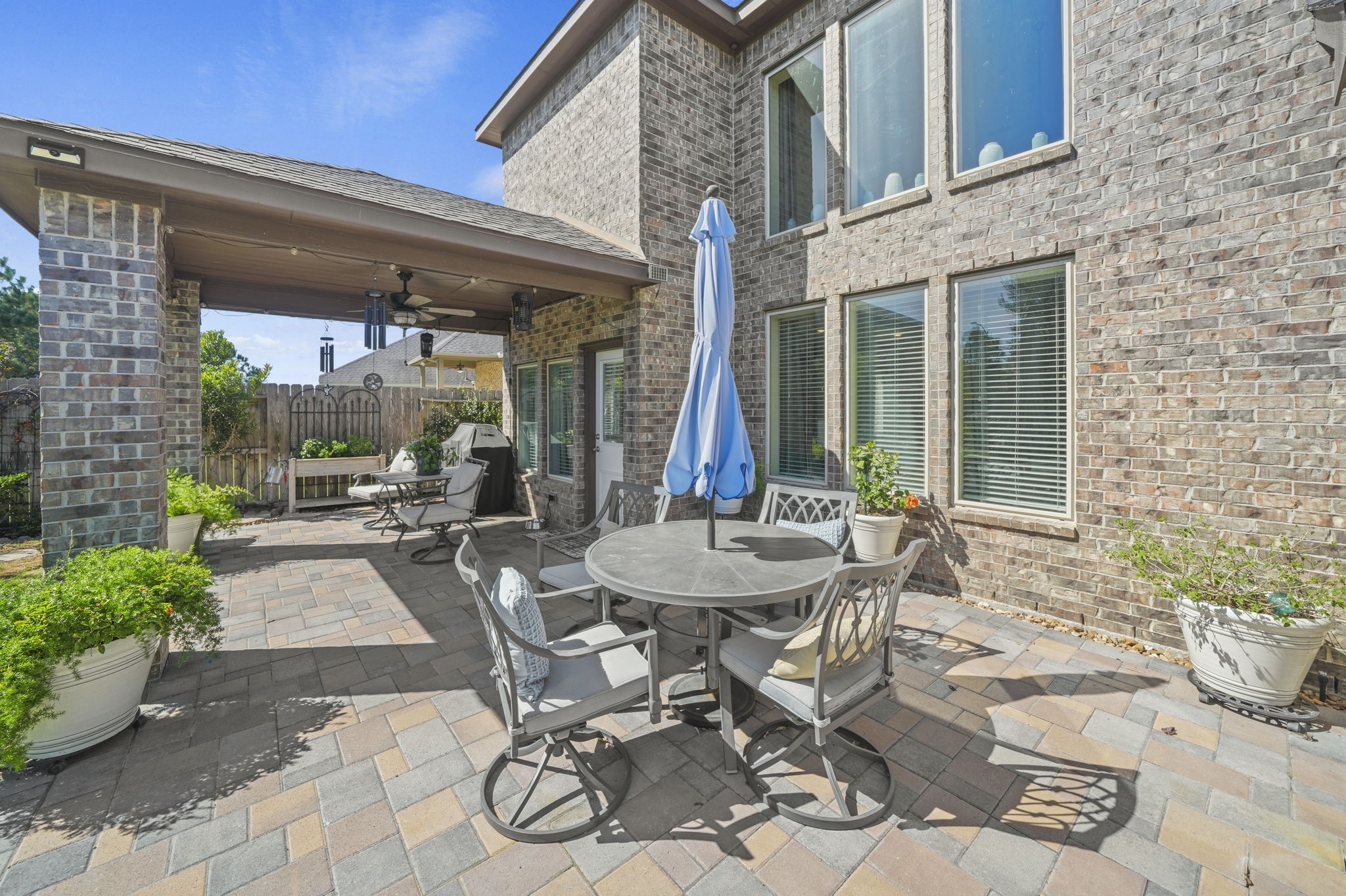Charming brick patio with ample seating, perfect for outdoor dining and relaxation, featuring a covered area and lush potted greenery.