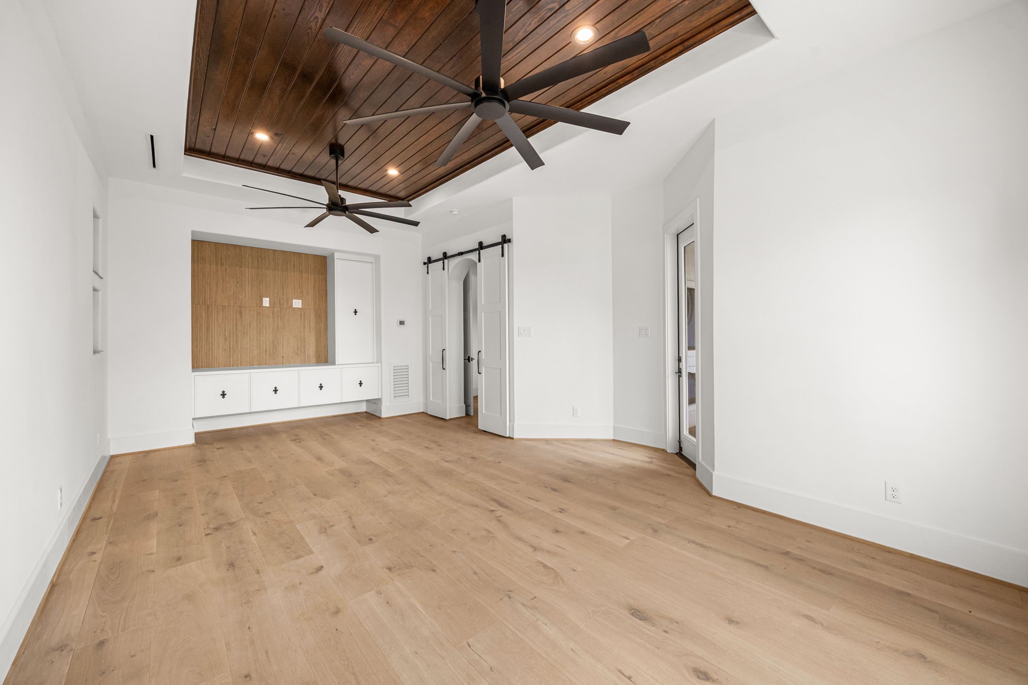 Another view highlights the custom floating cabinetry with dedicated TV space, complemented by stylish barn doors leading into the room.