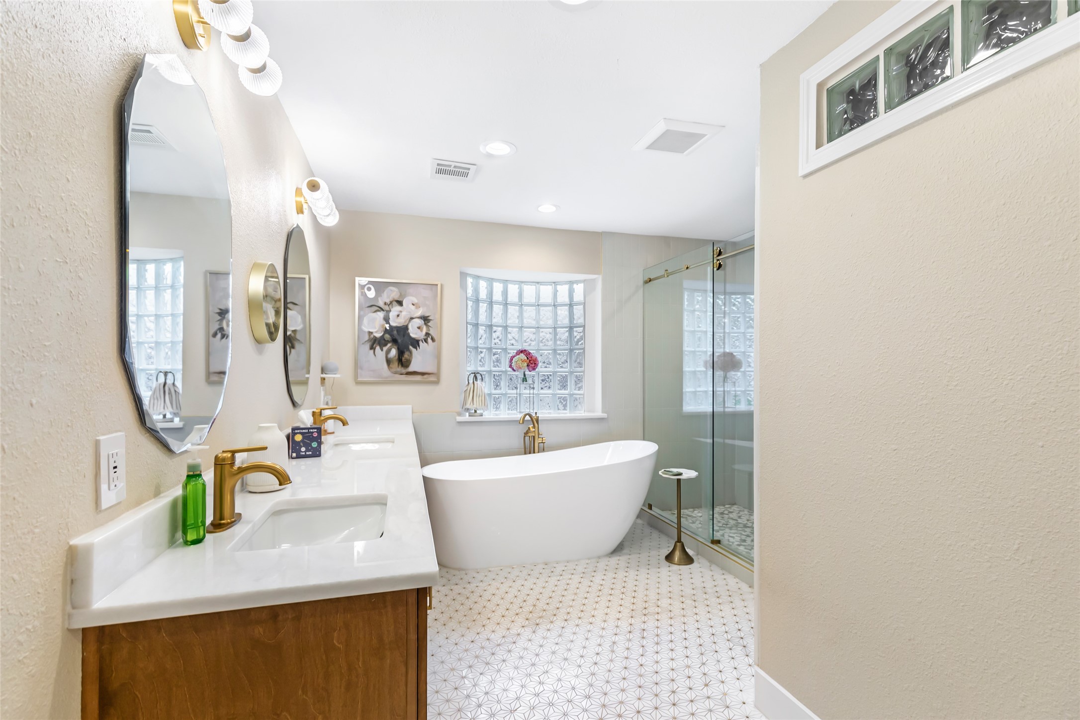 Luxurious bathroom featuring a sleek freestanding tub, dual vanity with gold fixtures, elegant mirrors, and a spacious glass-enclosed shower, all enhanced by soft lighting and stylish decor.
