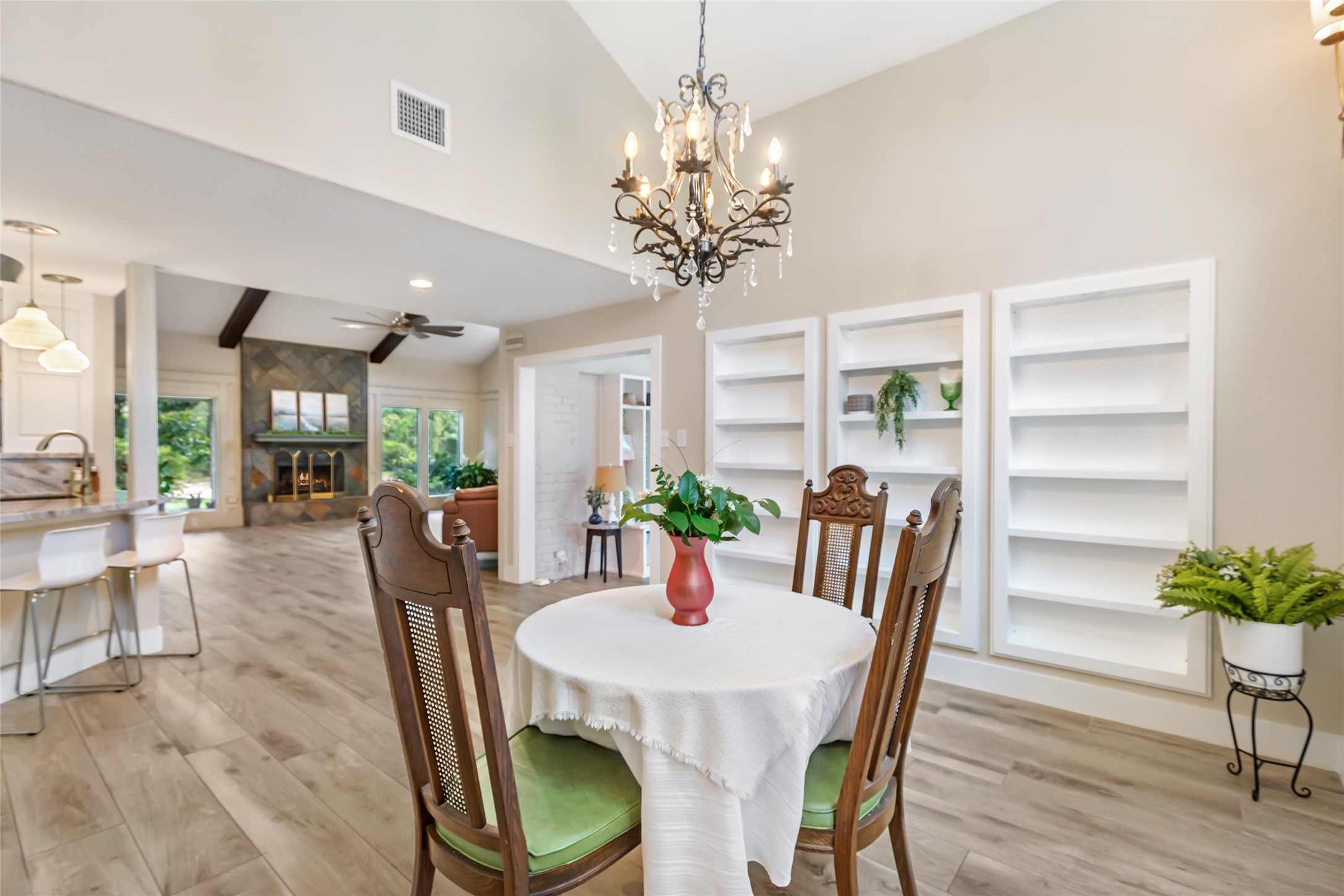 Elegant open-concept living space featuring a cozy dining area with a classic chandelier, built-in shelving, and a seamless flow into the bright kitchen and living room with a charming fireplace.