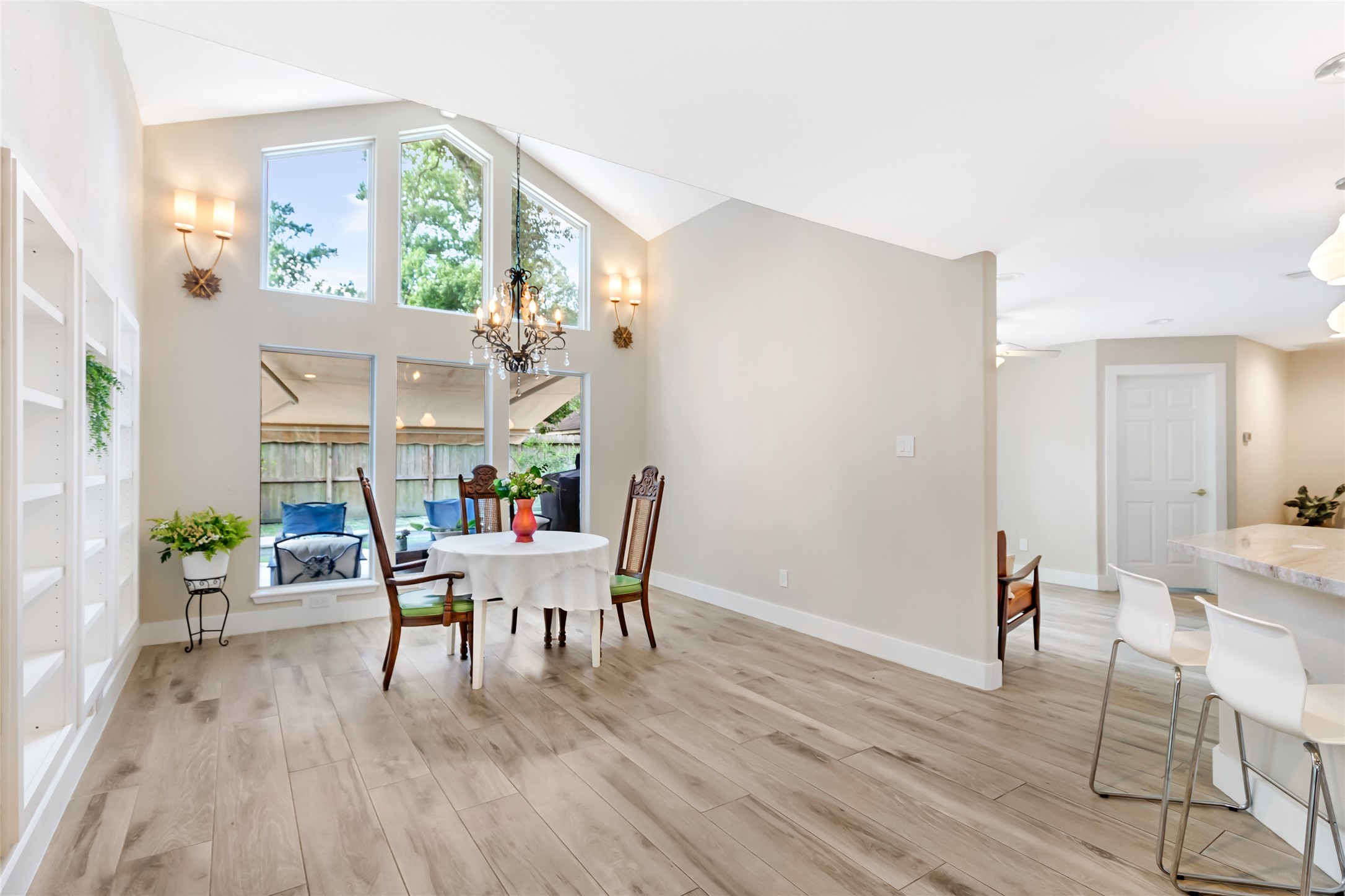 Bright and inviting dining area with high ceilings, large windows, and elegant chandelier, seamlessly connected to a modern kitchen with a breakfast bar.