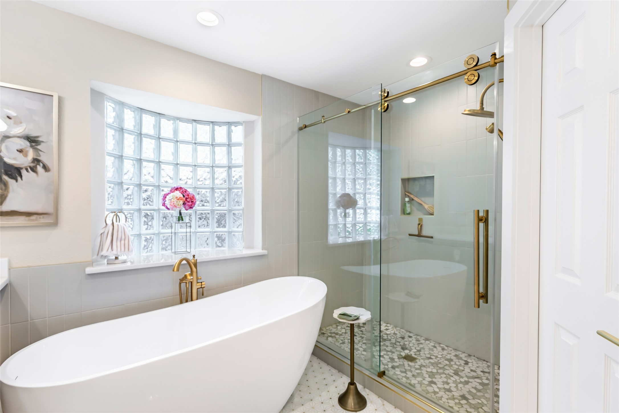 Luxurious bathroom featuring a sleek freestanding tub and elegant glass-enclosed shower, complemented by a stylish brass finish and a light-filled glass block window.