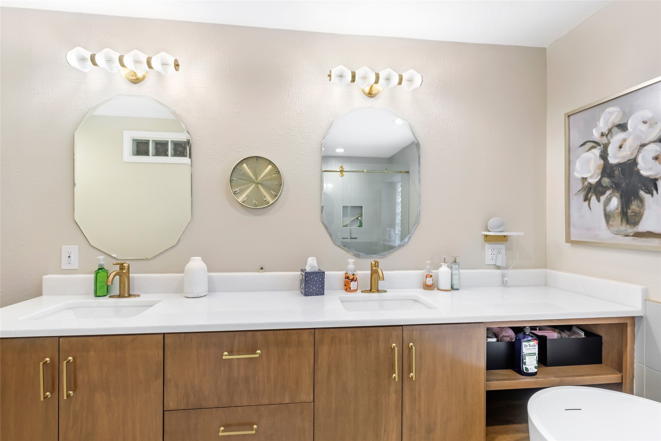 Elegant bathroom featuring dual sinks with sleek wooden cabinetry, modern gold fixtures, and chic hexagonal mirrors.