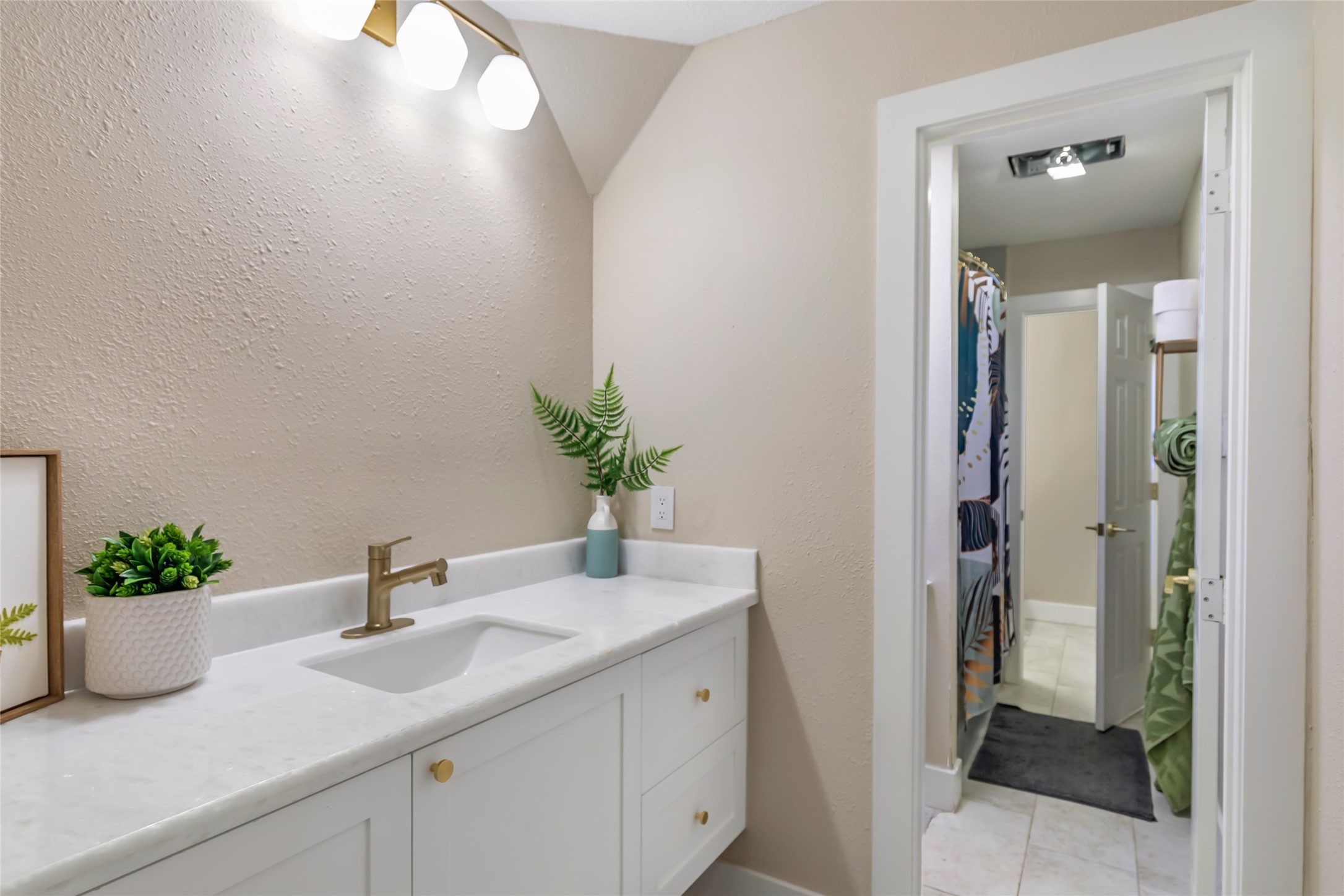 Modern jack-and-jill bathroom with a sleek white vanity, elegant gold fixtures, and soft lighting, leading to a well-lit shower area.