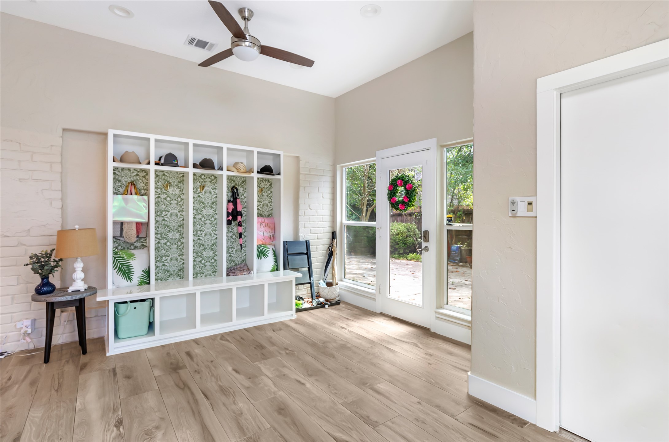 Bright and welcoming sunroom/mudroom featuring stylish built-in storage, leads into garage and has abundant natural light from large windows and a glass door leading to the outdoor pool area.