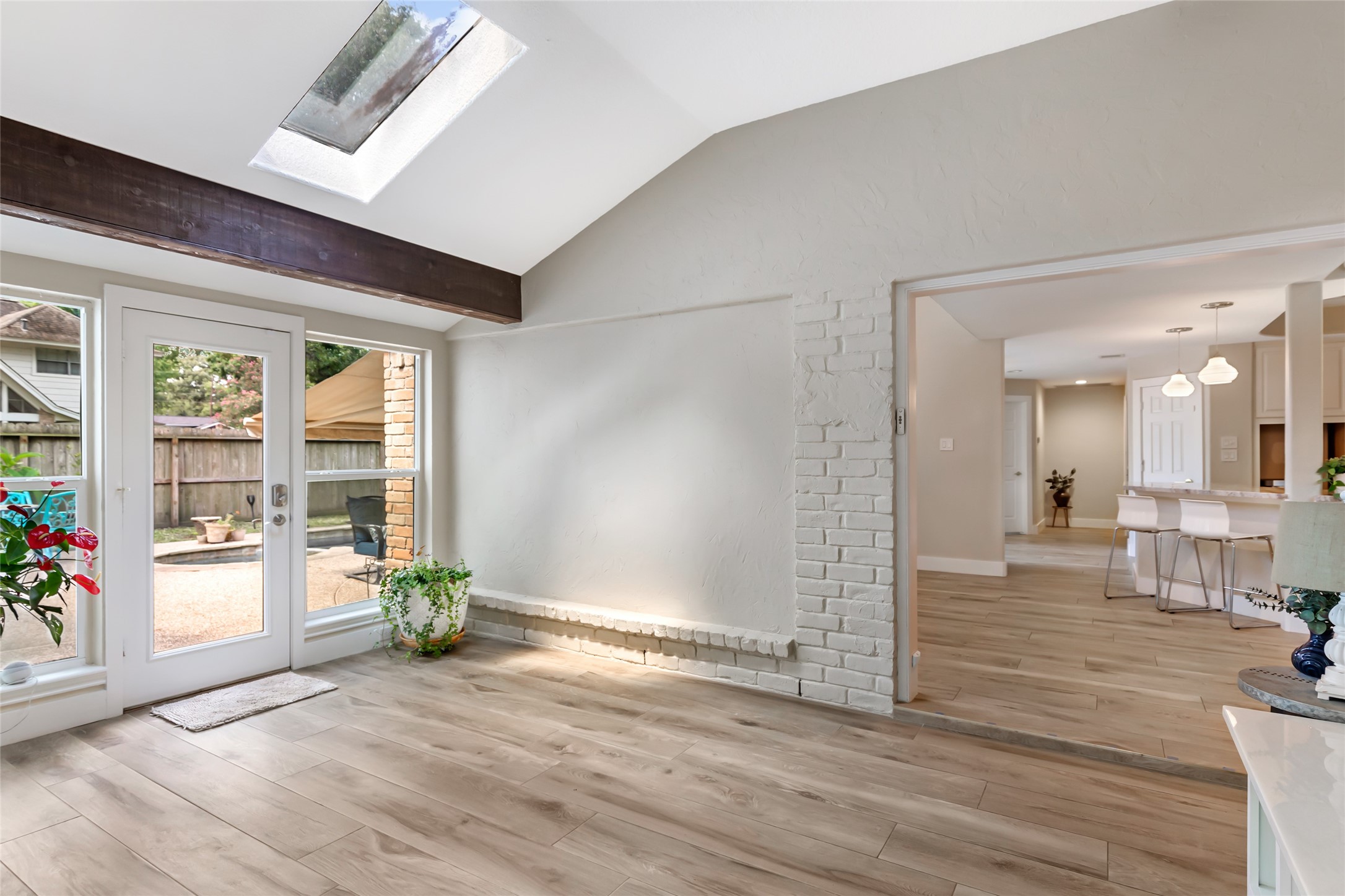 Bright and inviting sunroom with skylight, elegant wood flooring, and French doors leading to a serene patio. Open layout seamlessly connects to the modern kitchen and dining area.