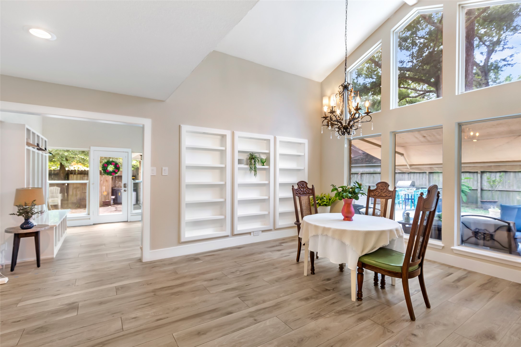 Bright dining area with high ceilings, elegant chandelier, built in shelves,  and expansive windows offering a view of the backyard.