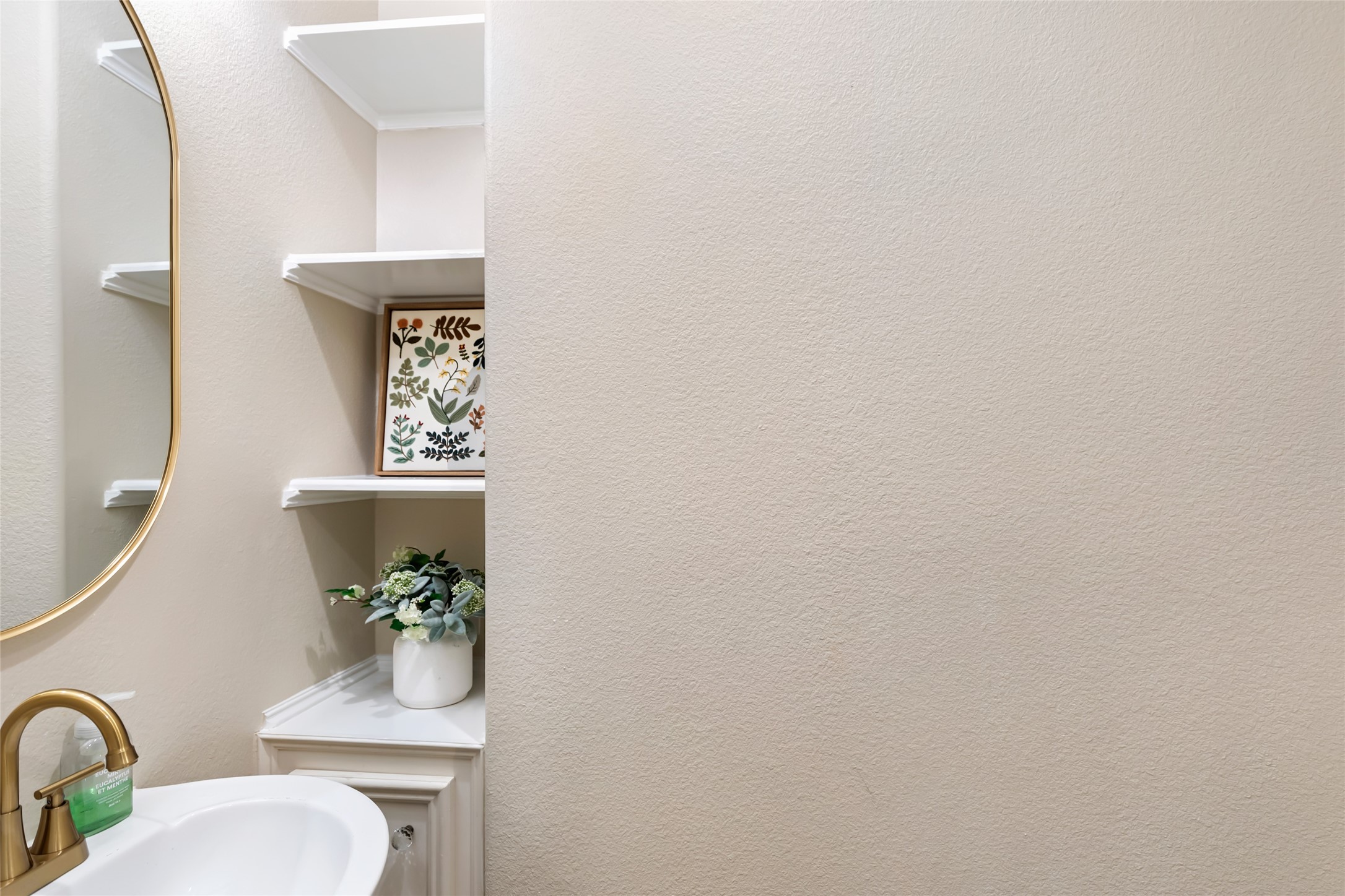 Elegant half bath with a modern gold faucet, sleek white sink, and stylish corner shelving for added decor and storage.