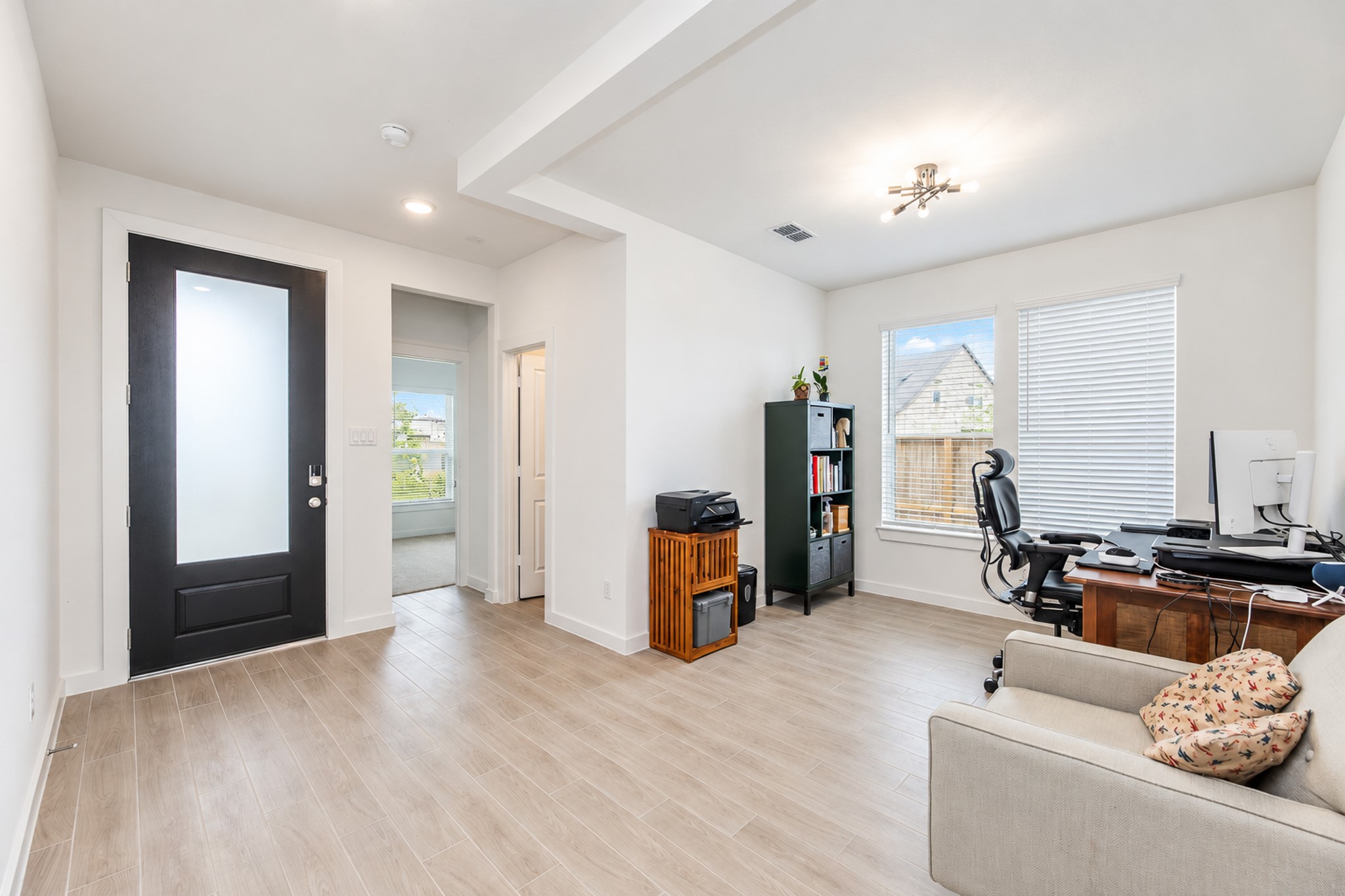 Bright and spacious office area with wood-look flooring, large windows for ample natural light, and a sleek modern front door. Perfect for a productive work-from-home setup.