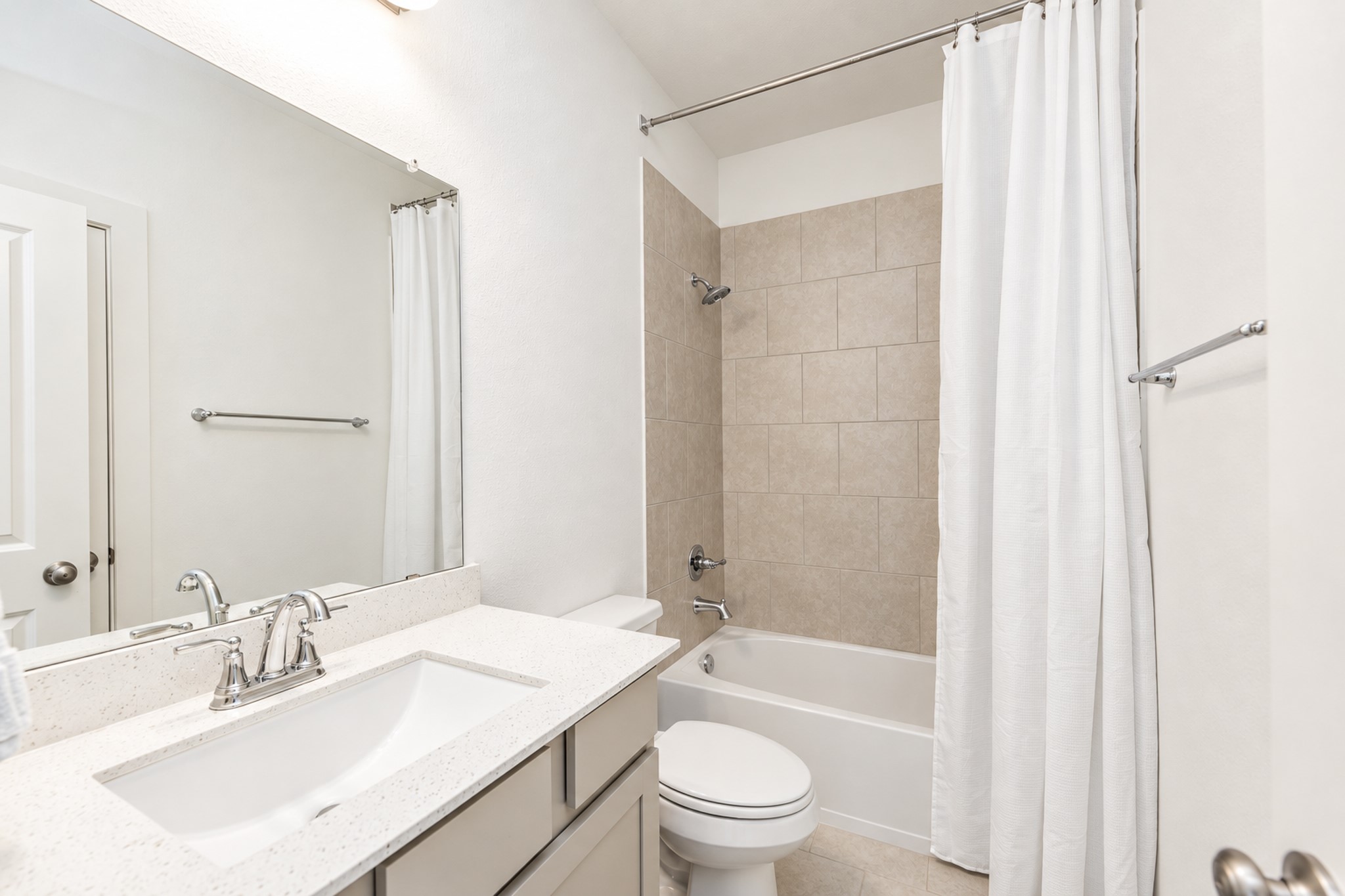 Bright and modern bathroom featuring a sleek vanity with ample counter space, a large mirror, and a classic shower-tub combination with neutral tile accents.