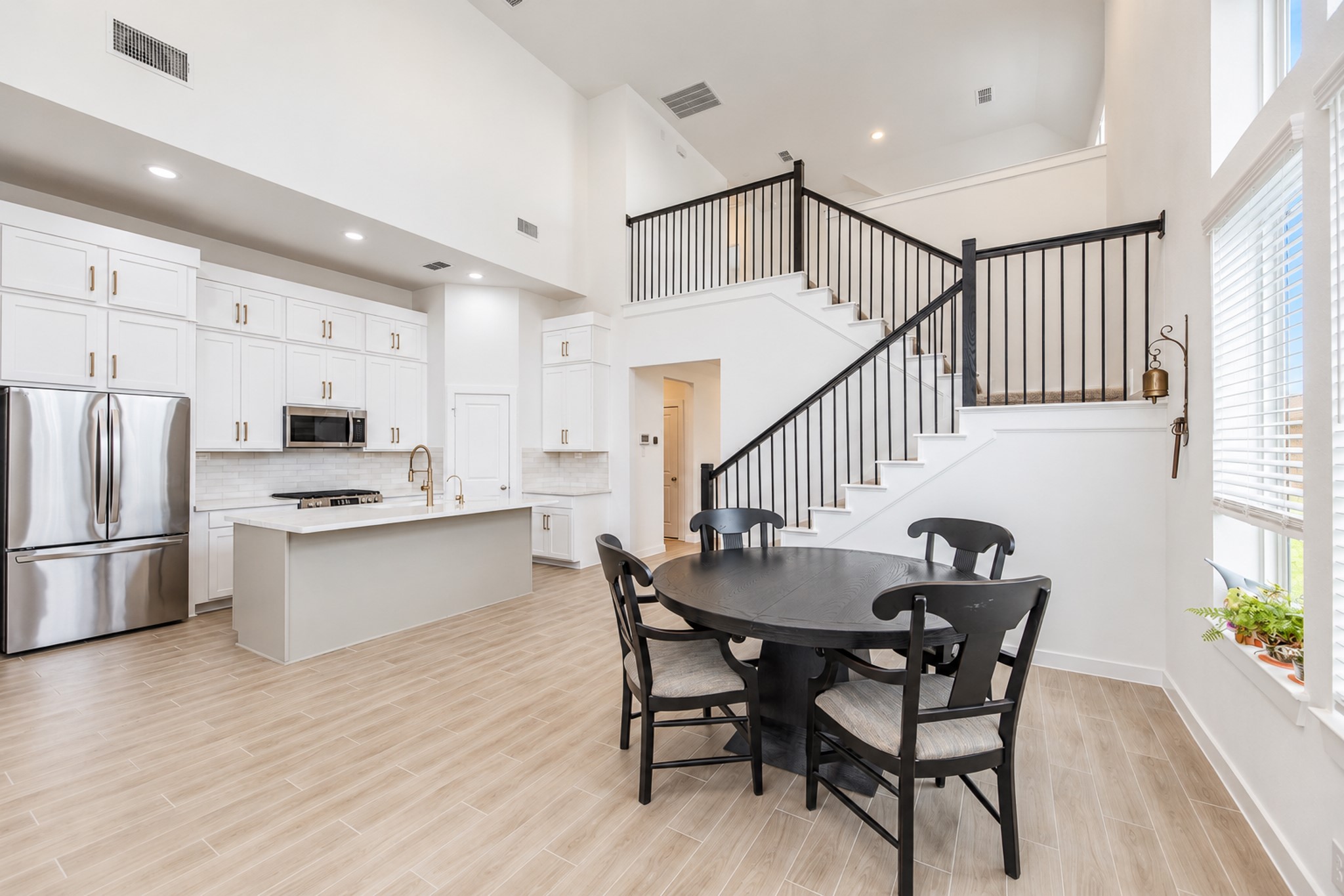 Spacious open-concept kitchen and dining area featuring high ceilings, modern cabinetry, stainless steel appliances, and a sleek island, complemented by a stylish staircase and large windows for natural light.