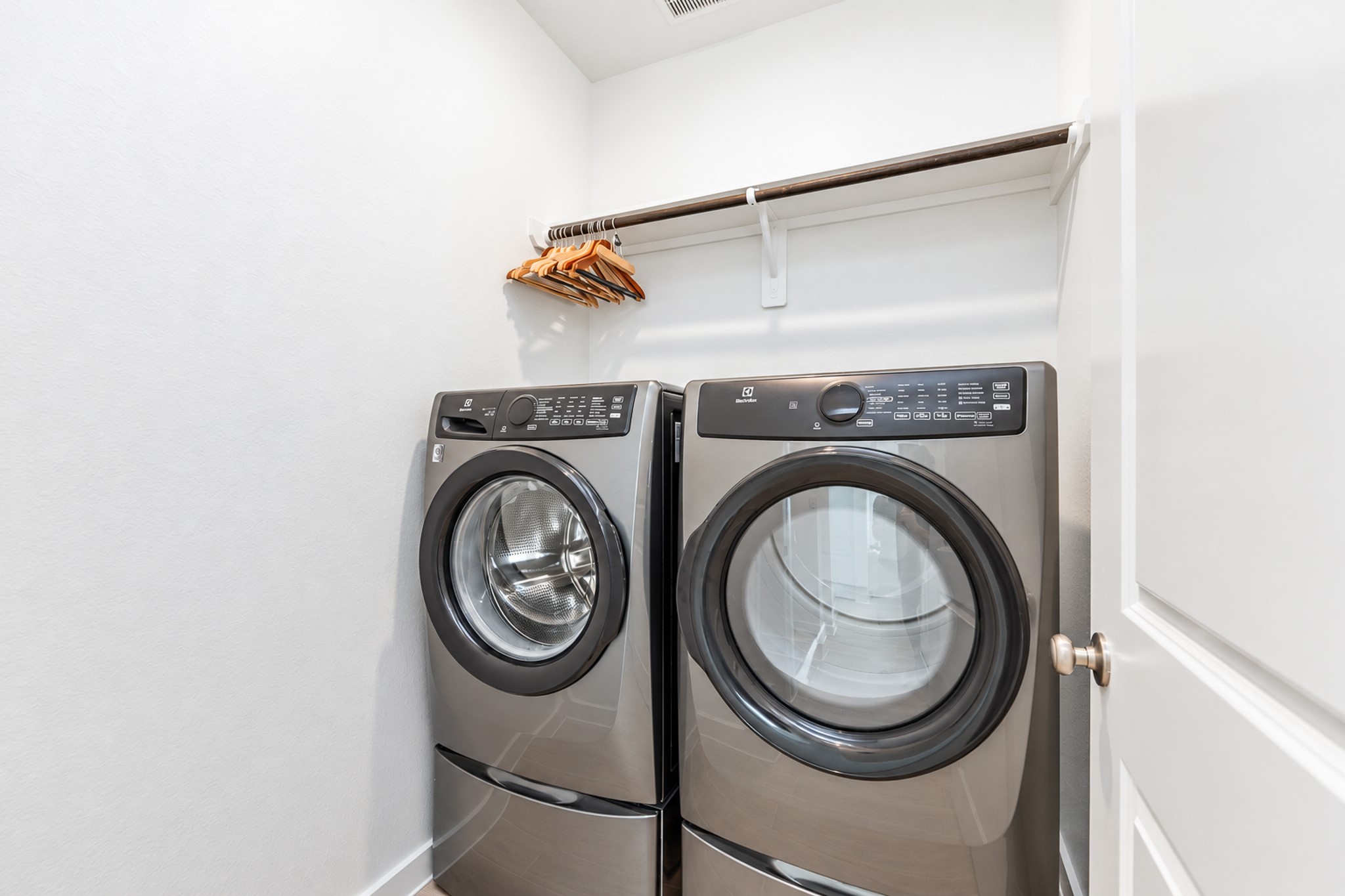 Modern laundry room featuring sleek front-loading washer and dryer, complemented by a convenient overhead shelf with hangers.
