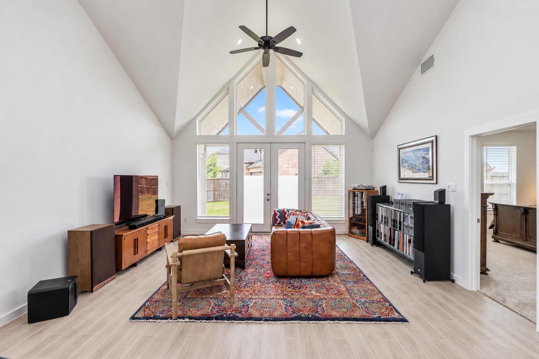 Spacious living room with soaring vaulted ceilings, abundant natural light from large windows, and stylish hardwood floors, creating a warm and inviting atmosphere.