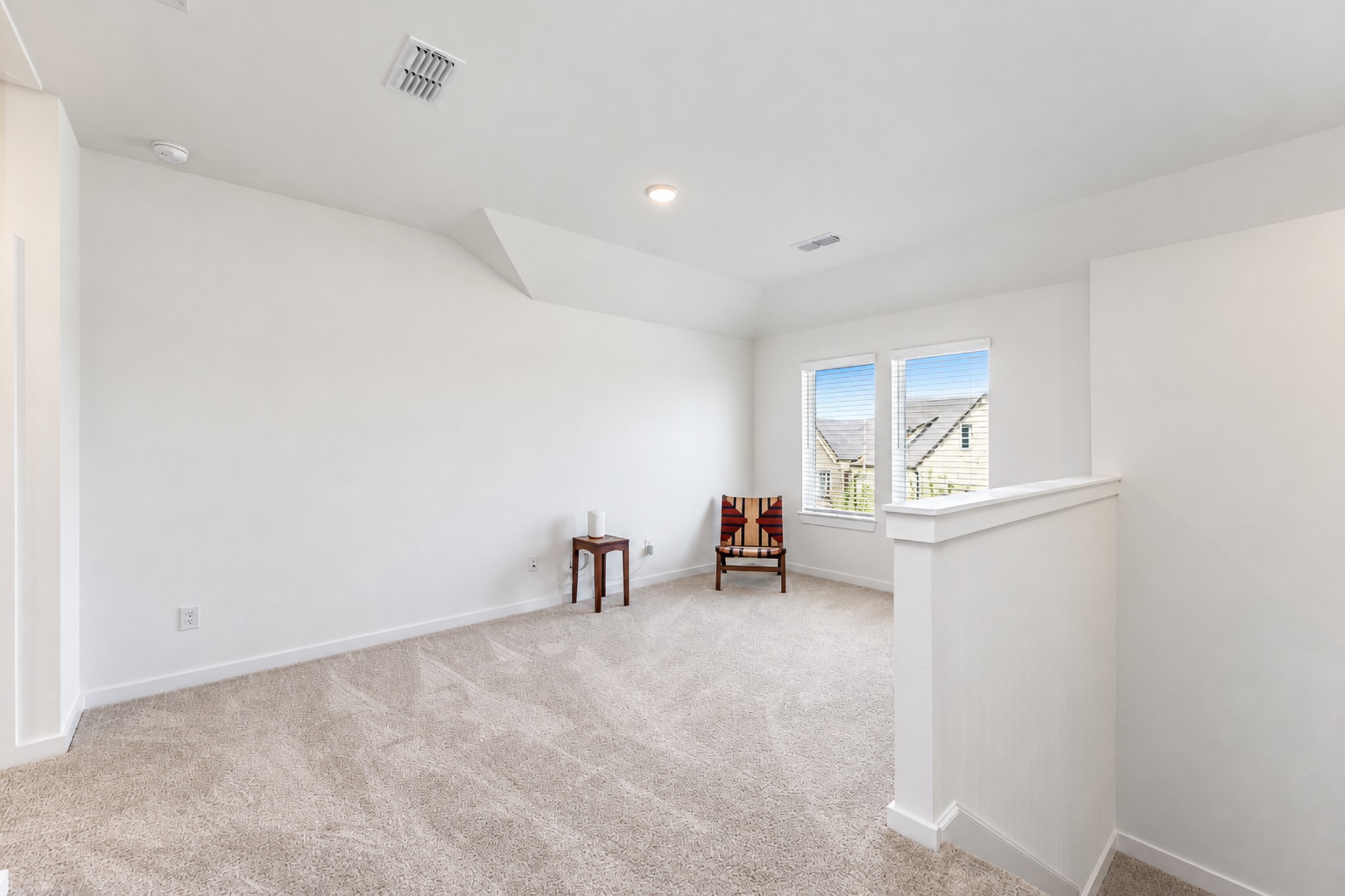 Bright and inviting loft space with plush carpeting, perfect for a cozy reading nook or office area, featuring two large windows for ample natural light.