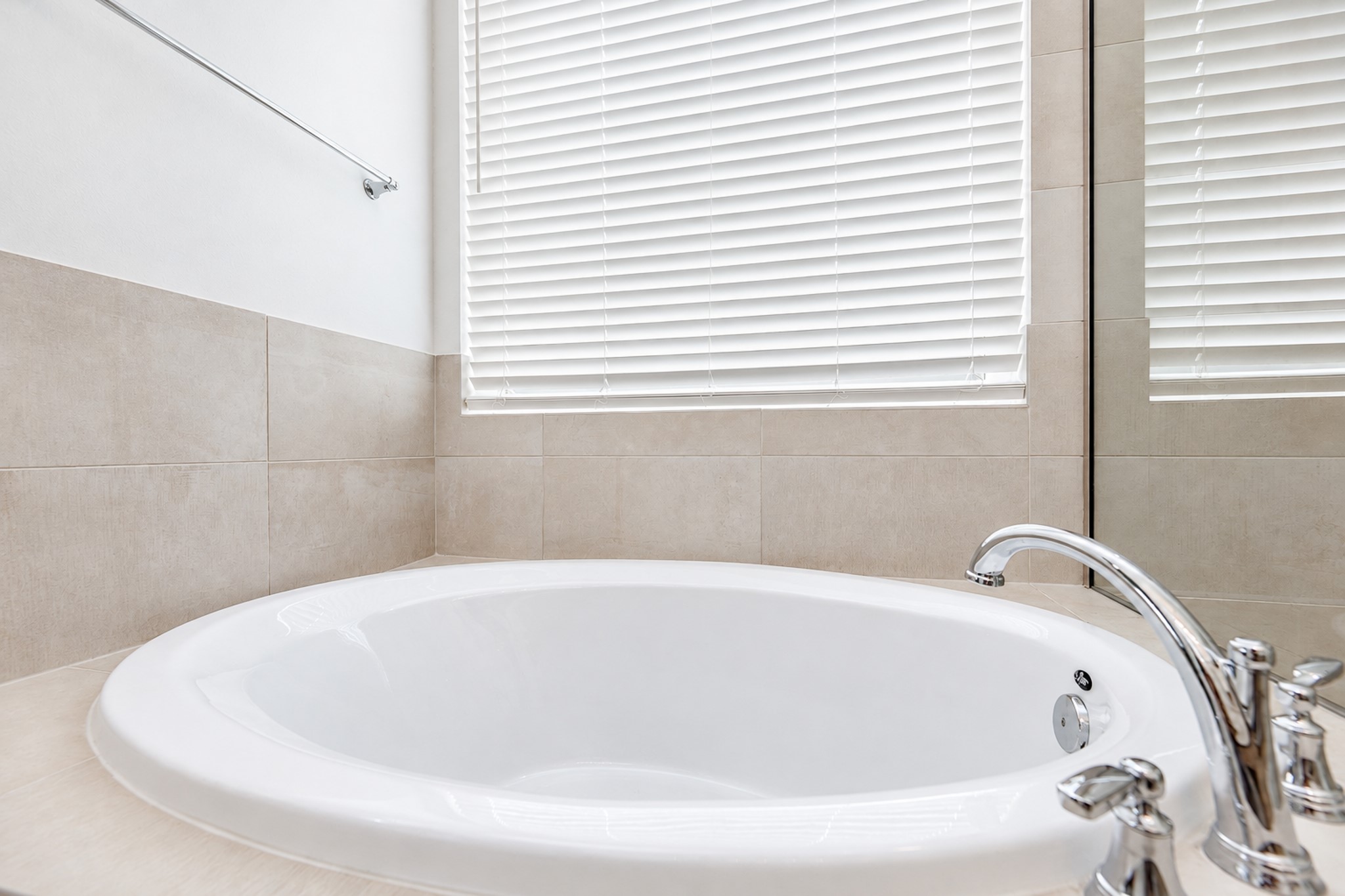 Luxurious bathroom featuring a spacious soaking tub with elegant fixtures, complemented by soft neutral tiles and ample natural light.