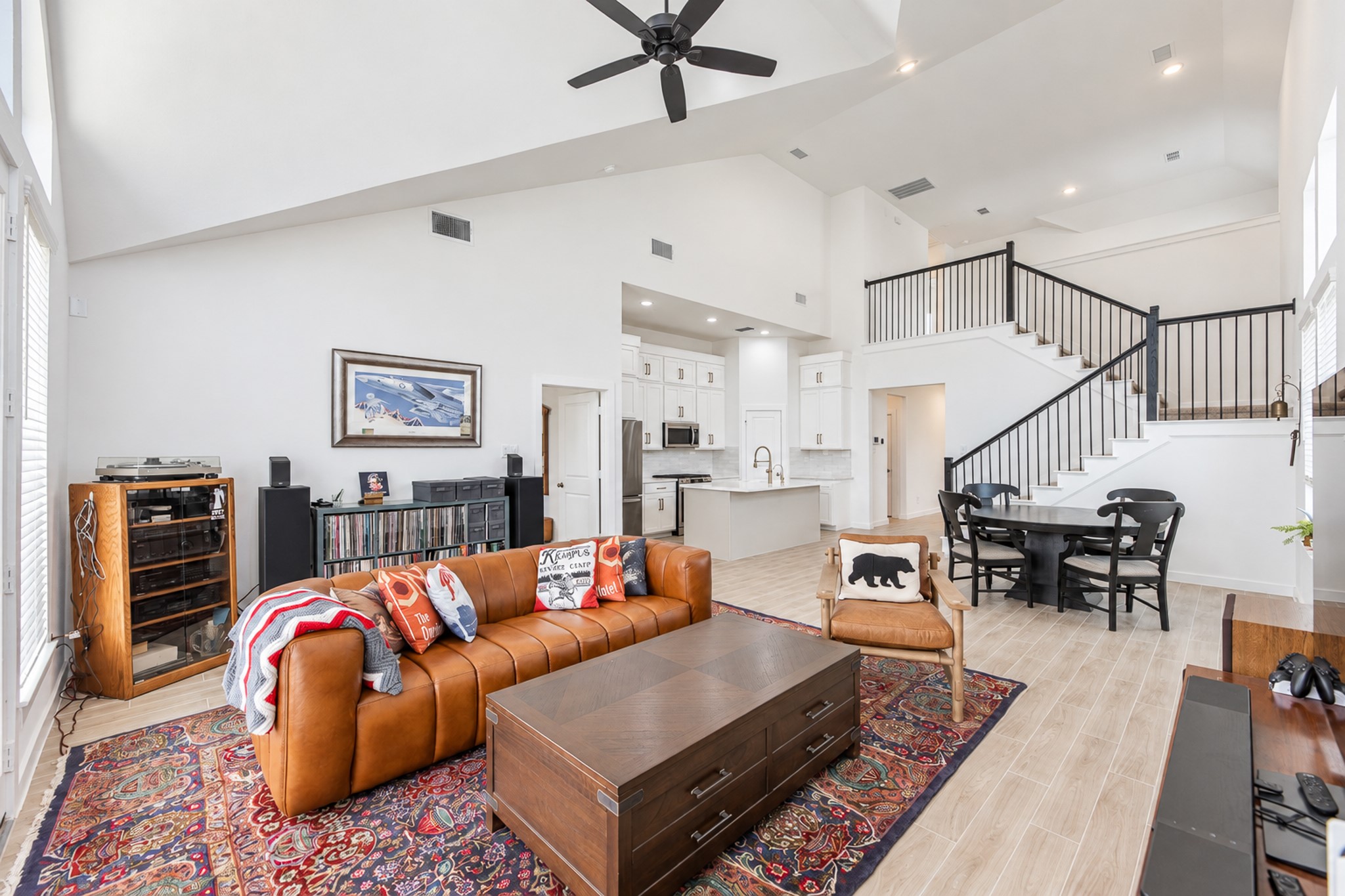 Spacious open-concept living area featuring a vaulted ceiling, elegant staircase, and a modern kitchen with a large island. Natural light floods through expansive windows, highlighting the stylish decor and inviting atmosphere.