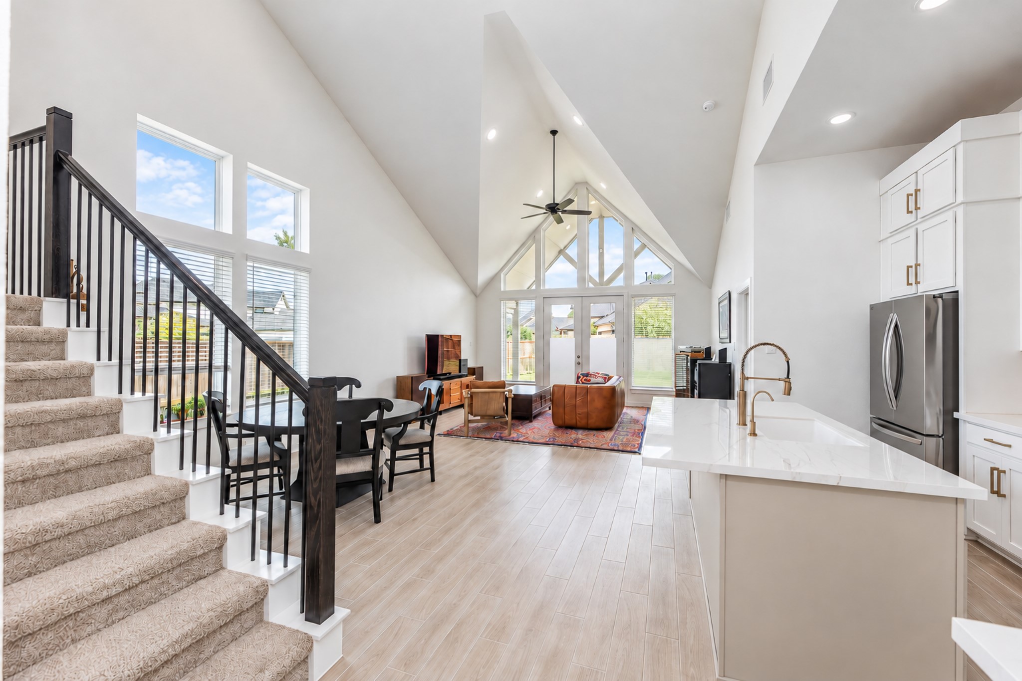 Stunning open-concept living area with soaring vaulted ceilings, large windows for natural light, and modern finishes. The kitchen features sleek countertops and stainless steel appliances, seamlessly flowing into a cozy seating area and dining space.