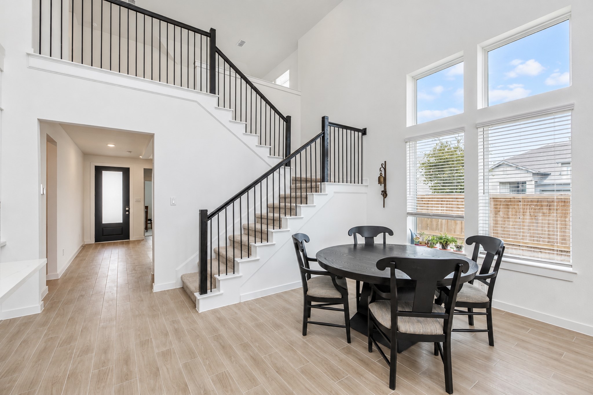 Bright and airy dining area with large windows and high ceilings, featuring a modern staircase and open layout.