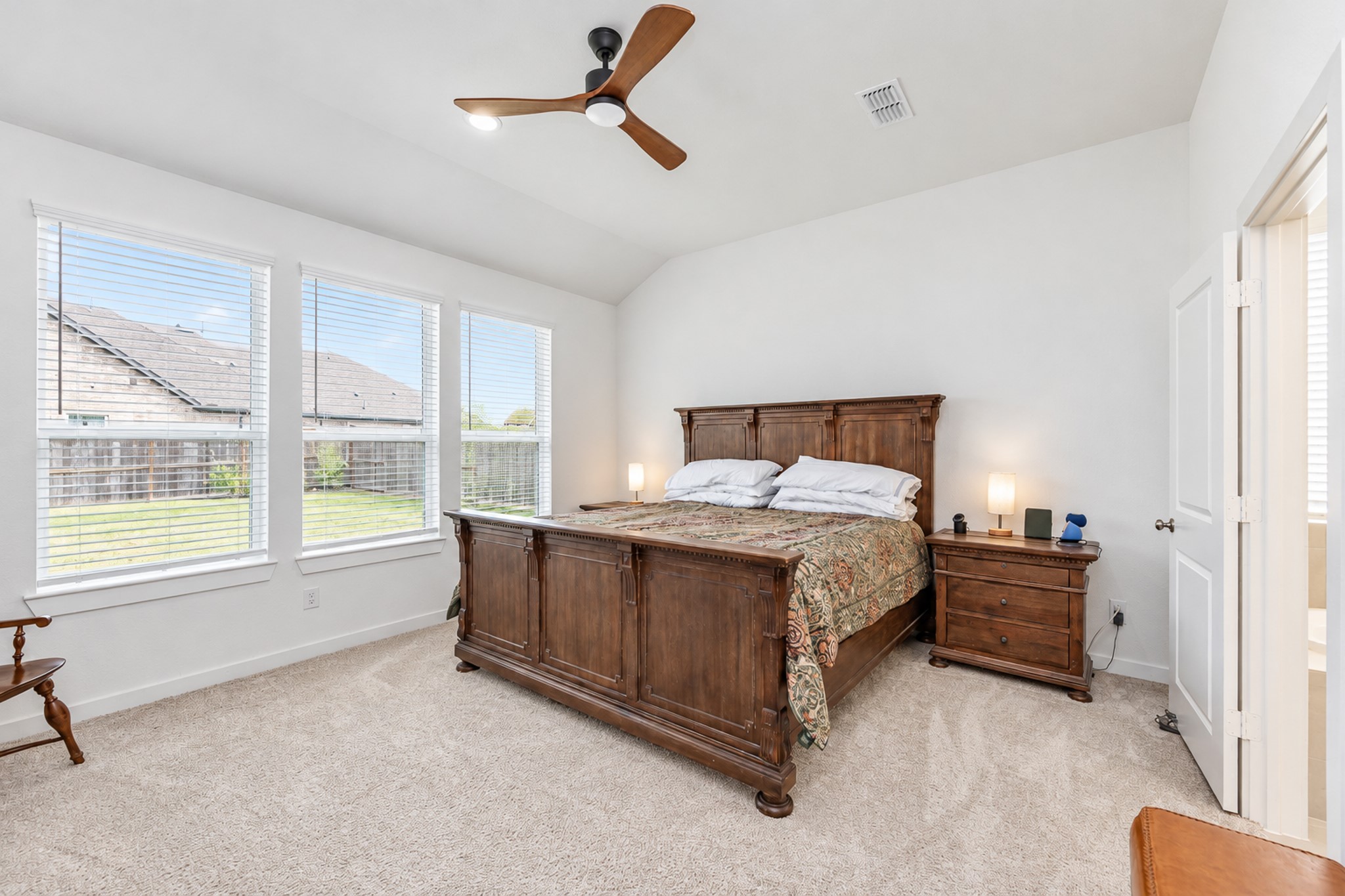Spacious bedroom with vaulted ceiling, featuring abundant natural light from large windows, and a cozy atmosphere with a classic wooden bed and matching nightstand.