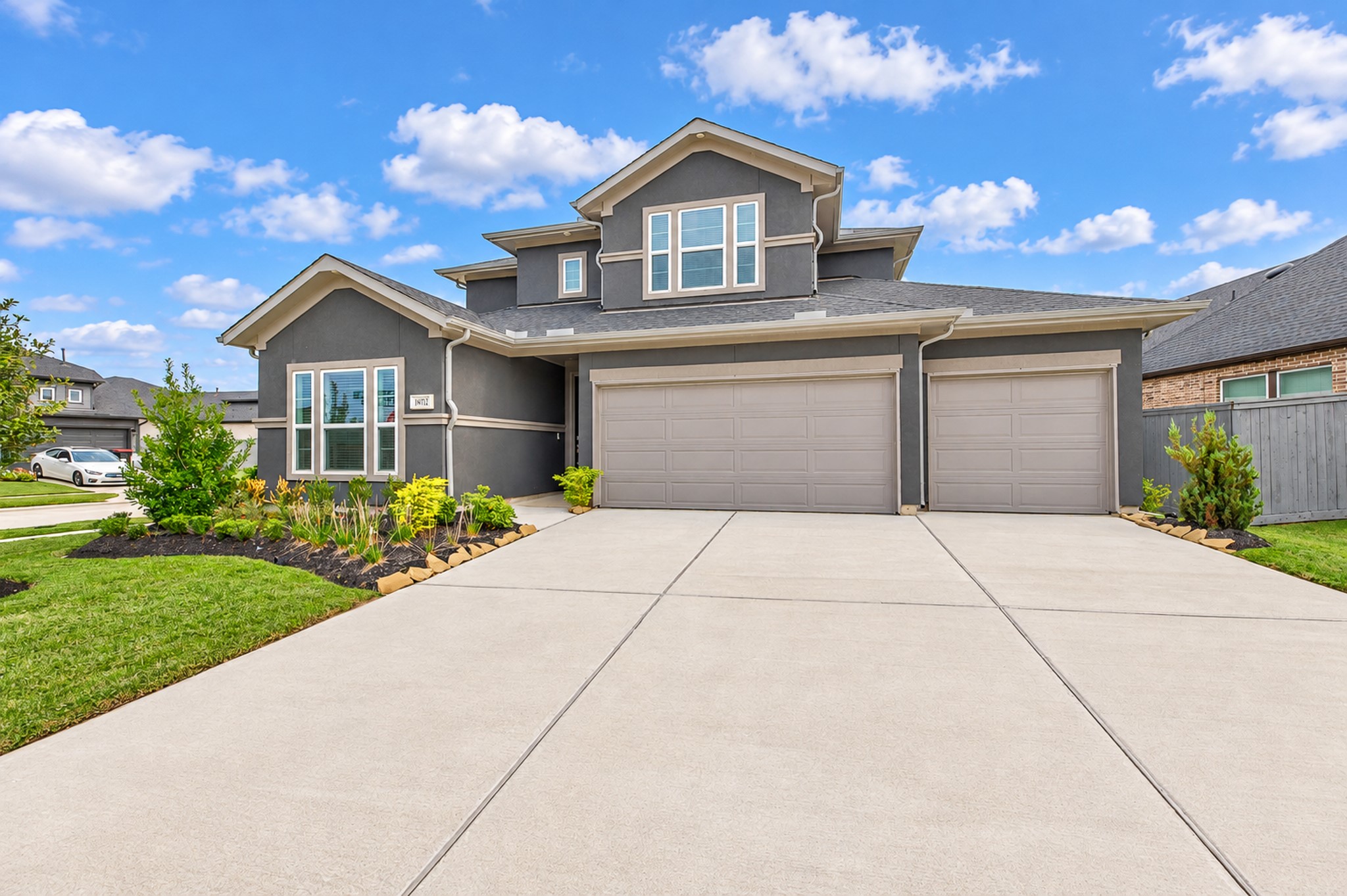Stunning modern home with a spacious three-car garage, manicured landscaping, and a sleek gray exterior, perfect for family living.