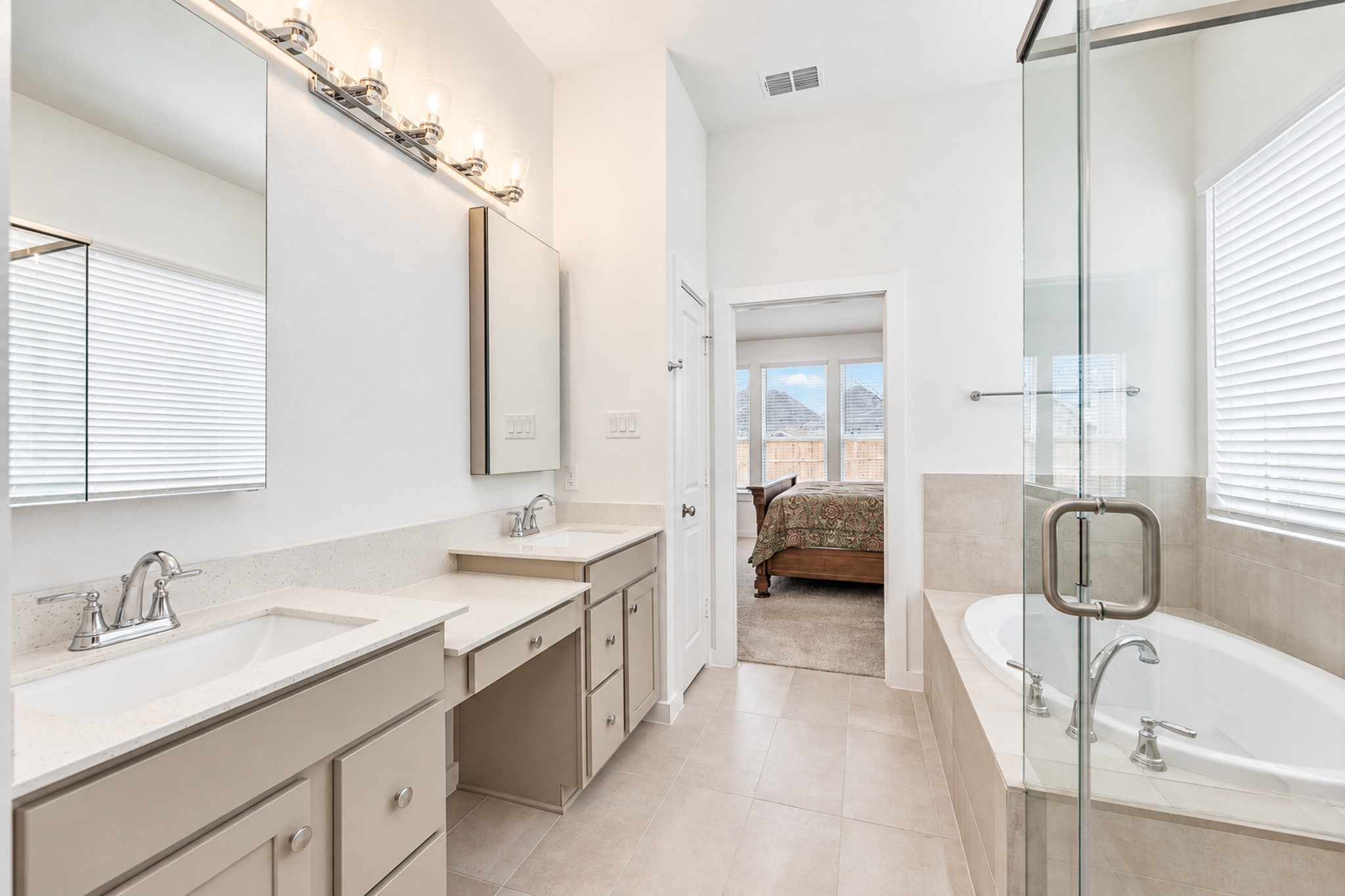 Bright and spacious bathroom featuring dual sinks, ample cabinetry, a luxurious soaking tub, and a glass-enclosed shower, seamlessly connecting to the bedroom.