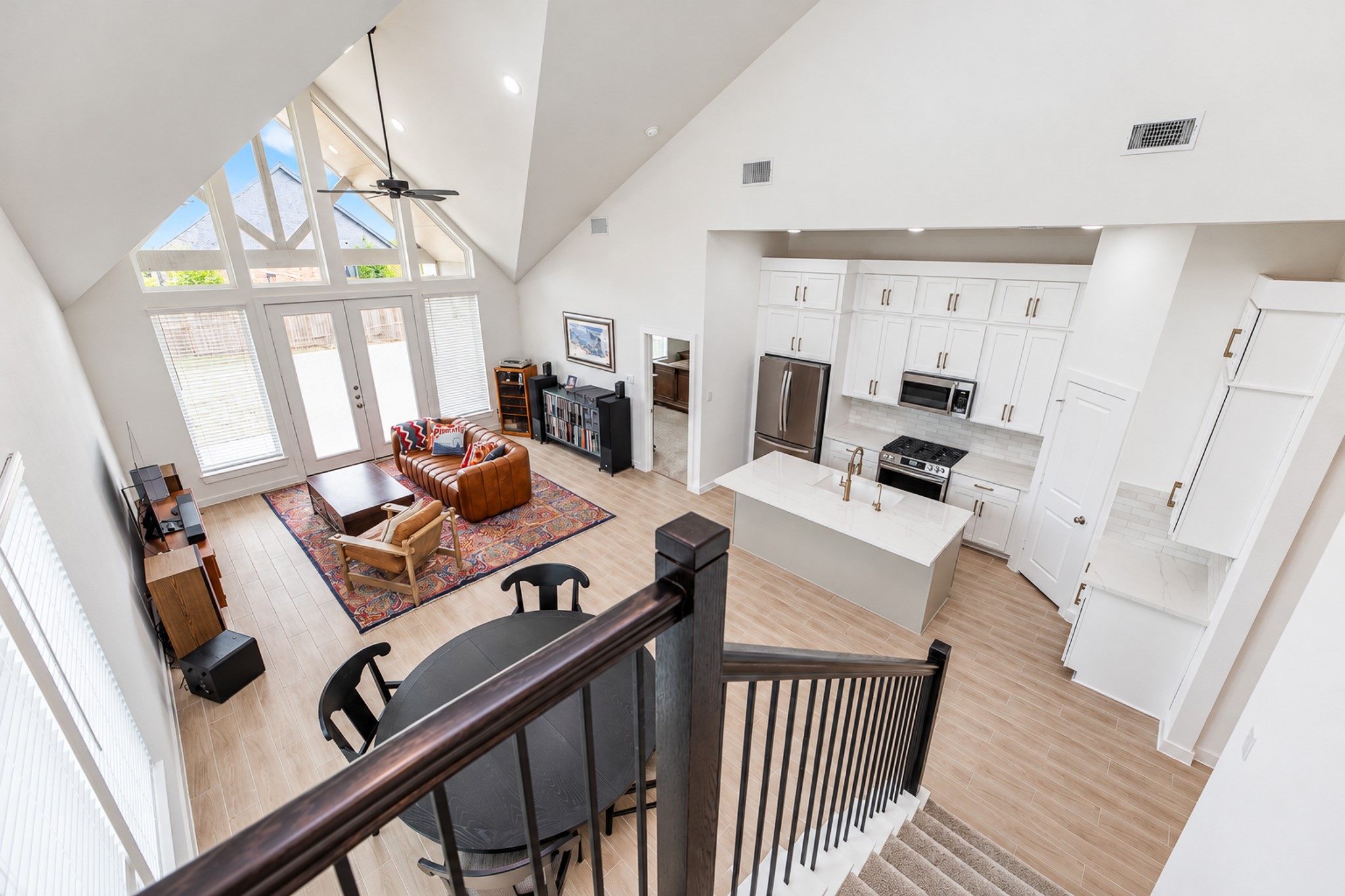 Stunning open-concept living space with soaring vaulted ceilings, abundant natural light from large windows, and a modern kitchen featuring sleek cabinetry and stainless steel appliances.