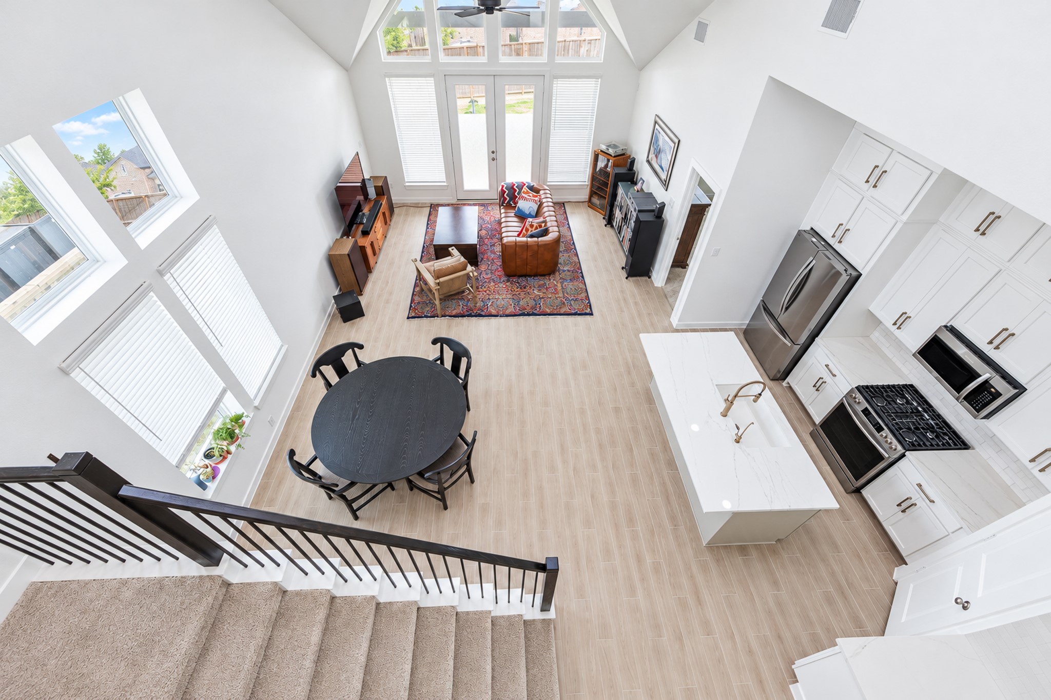 Spacious and bright open-concept living area with soaring ceilings, modern kitchen featuring stainless steel appliances, and abundant natural light from large windows.