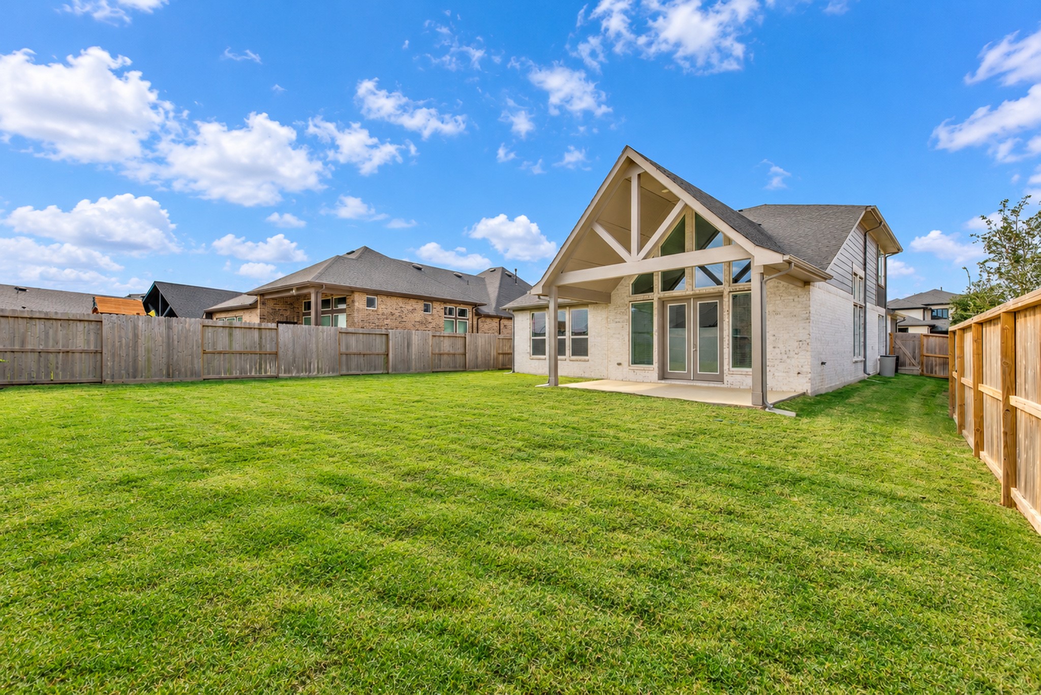 Spacious backyard with lush green lawn, perfect for outdoor activities, featuring a charming covered patio and modern architectural details.
