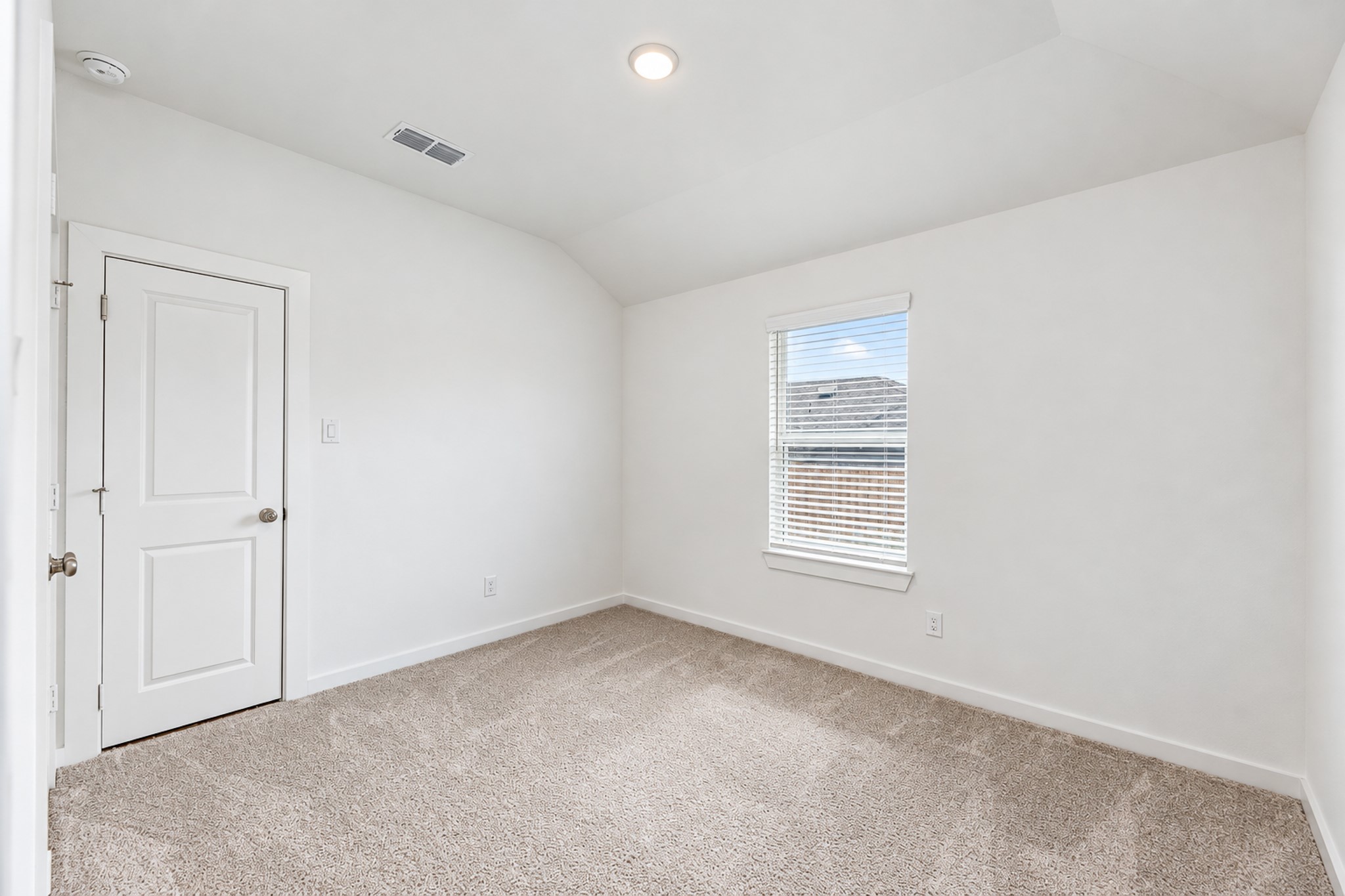 Cozy and bright bedroom with soft carpeting, a large window for natural light, and a classic white door.