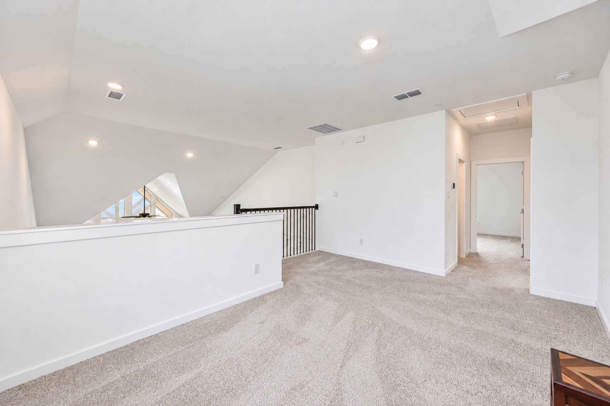 Spacious upper-level landing with plush carpeting and recessed lighting, offering access to additional rooms and featuring a modern railing detail.