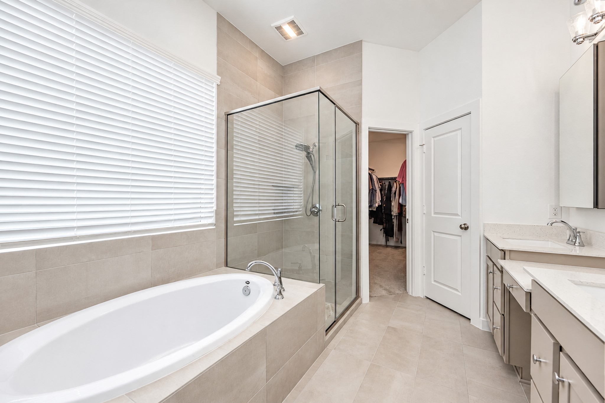 Elegant bathroom featuring a spacious glass-enclosed shower, luxurious soaking tub, dual vanities, and access to a walk-in closet.