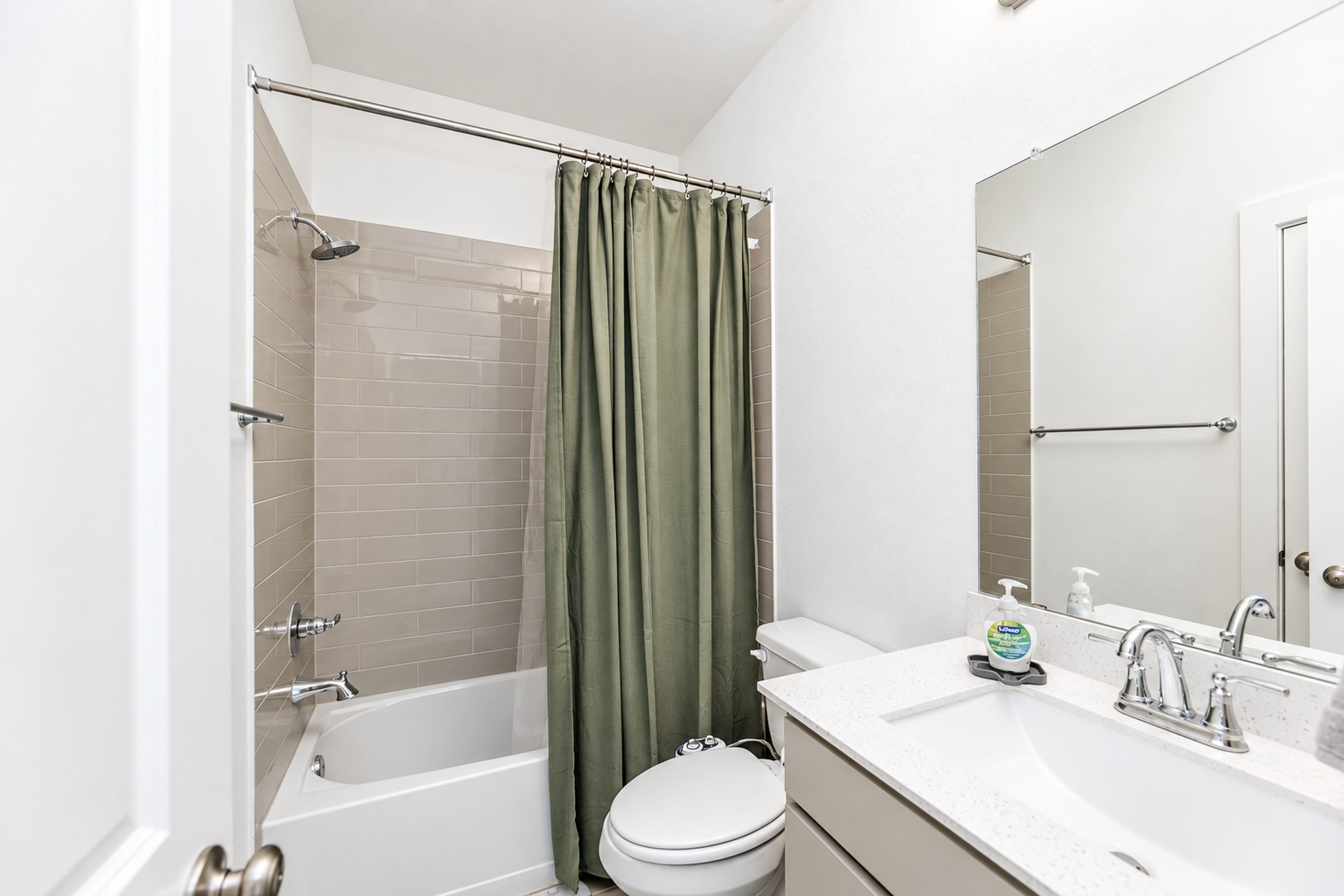 Bright and modern bathroom featuring a sleek vanity with a polished countertop, a full bathtub with a tiled shower, and a contemporary shower curtain for added privacy.