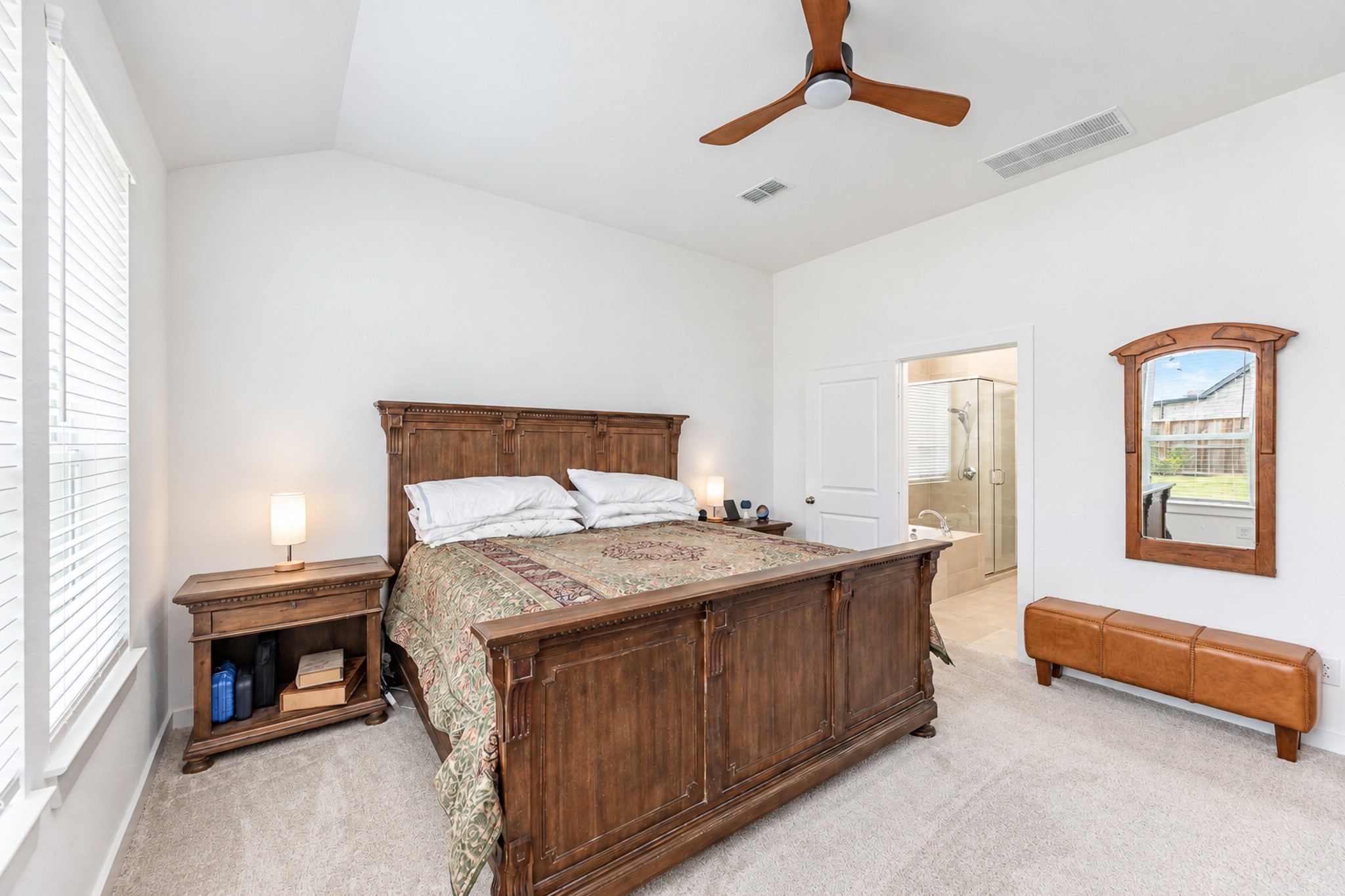 Spacious bedroom with a vaulted ceiling, natural light, and a classic wood bed set, leading to an en-suite bathroom.