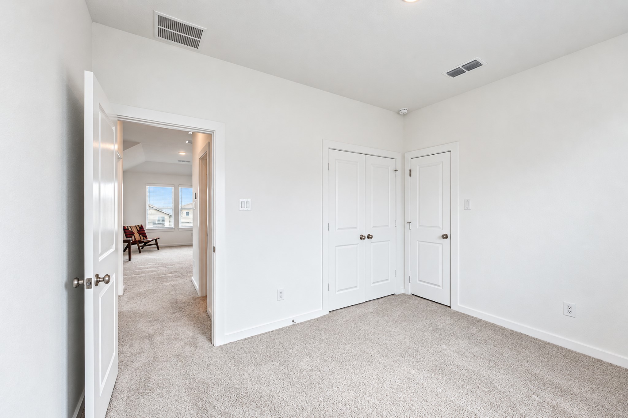 Bright and inviting bedroom with plush carpeting, dual closets, and an adjoining space leading to a sunlit room.