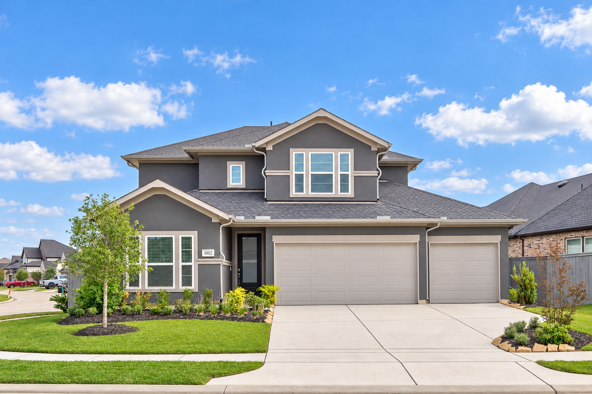 Stunning two-story home with a modern gray facade, three-car garage, and beautifully landscaped front yard on a corner lot.