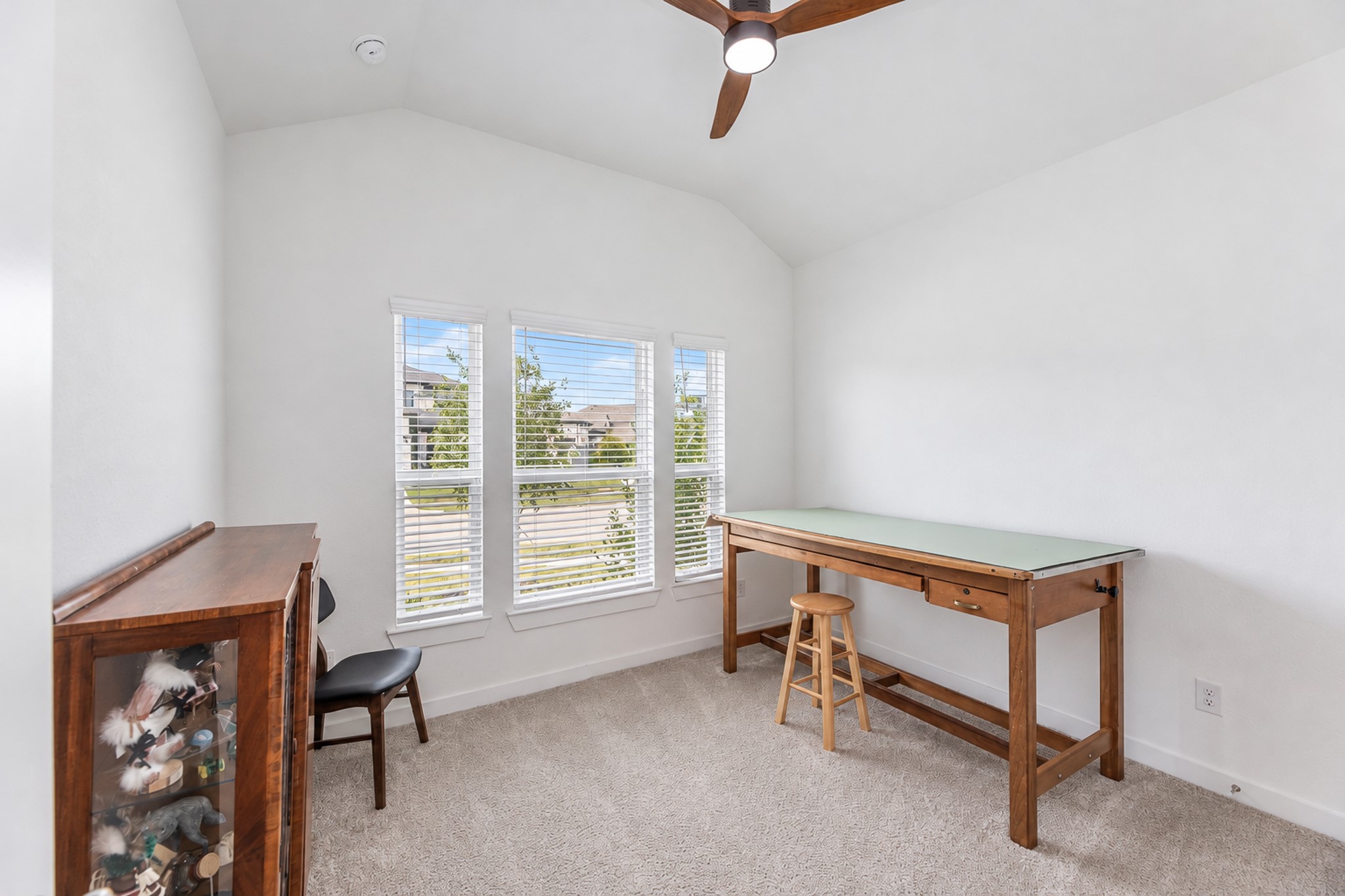 Bright and versatile room with high ceilings, large windows, and neutral carpeting, perfect for a home office or creative space.
