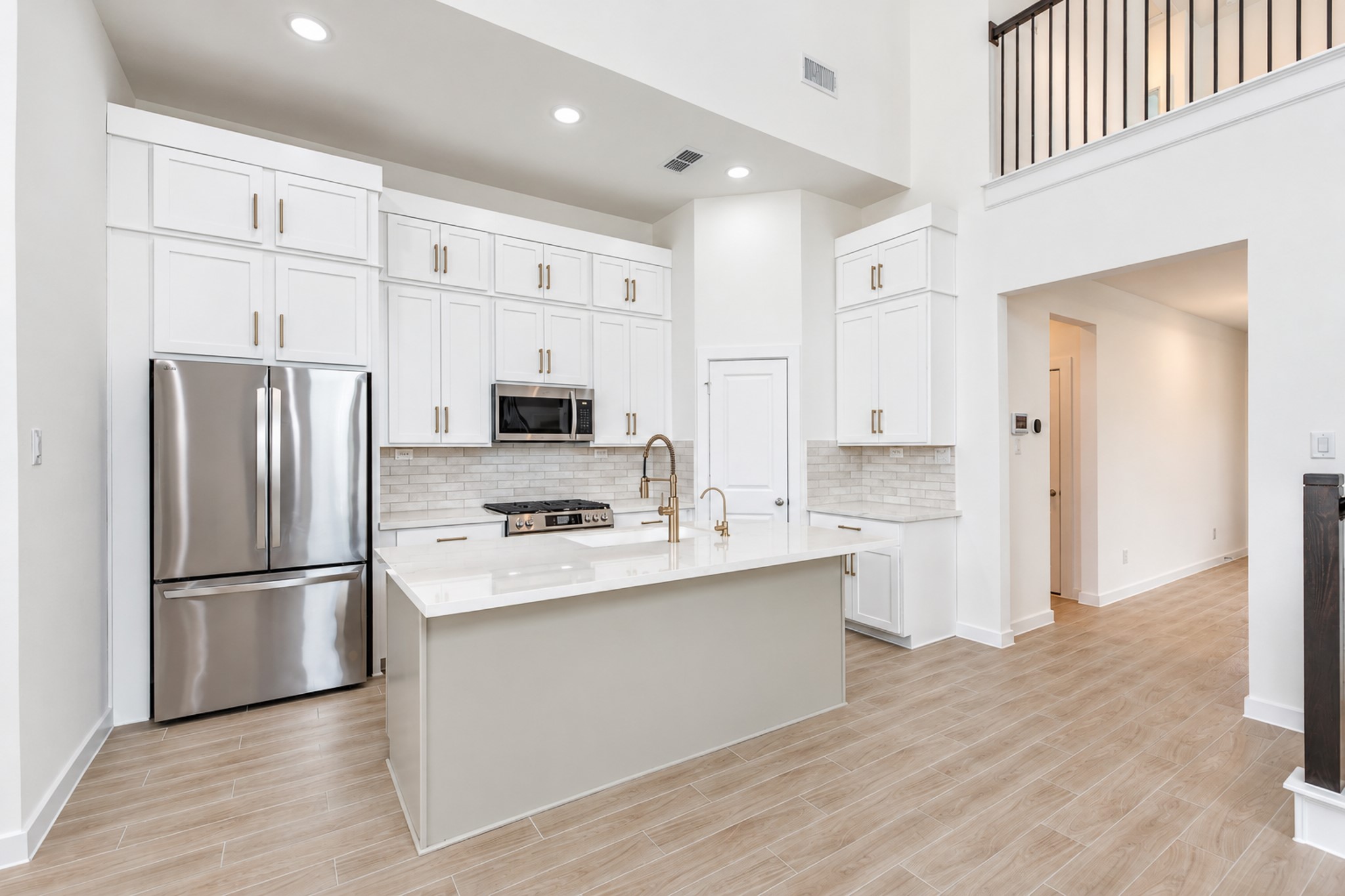 Elegant kitchen with high ceilings, modern stainless steel appliances, and sleek white cabinetry. The spacious island and stylish backsplash complement the warm wood-look flooring.