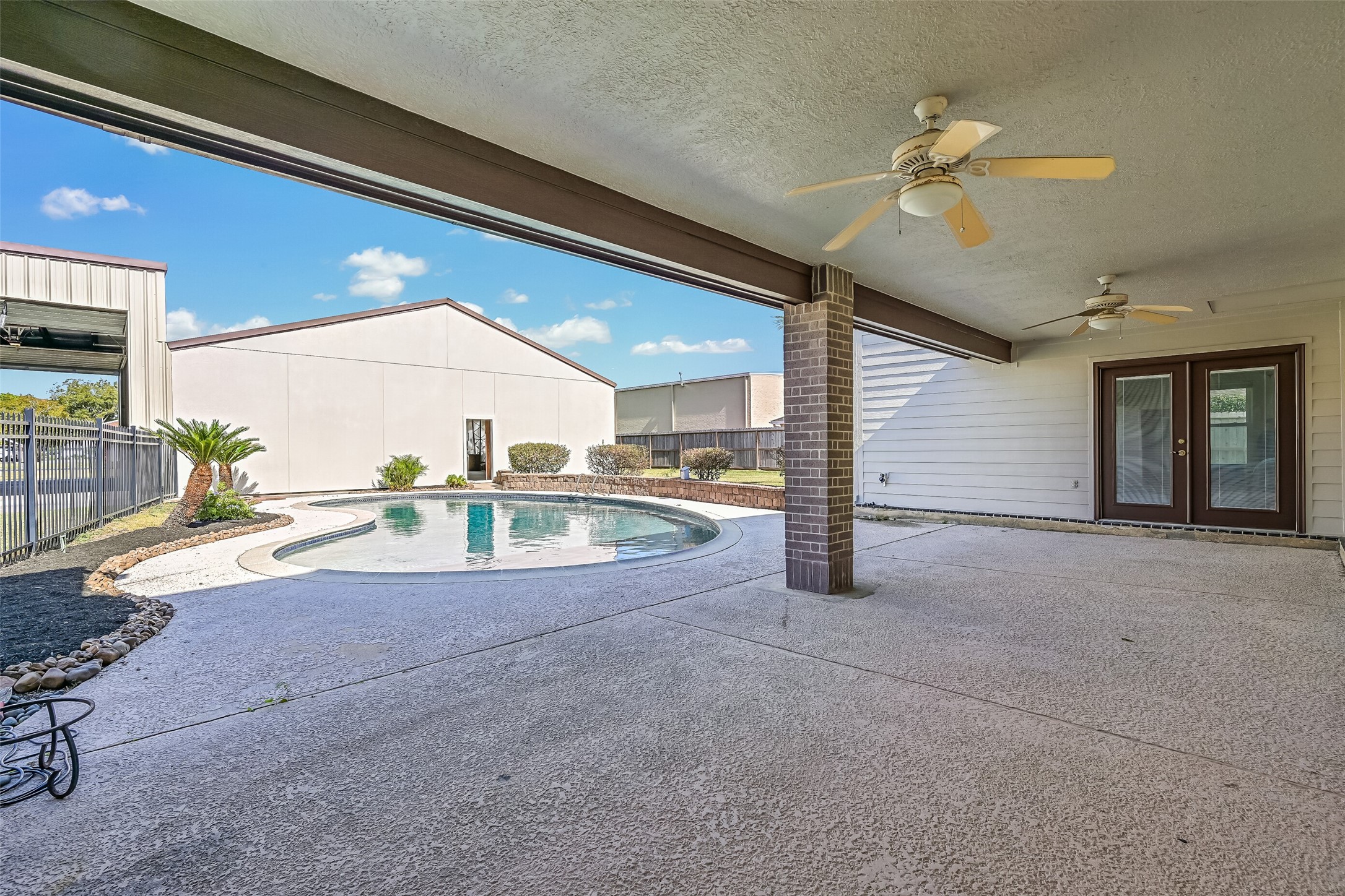 The expansive covered patio stretches along the rear of the home, offering a shaded setting for outdoor dining, relaxing or gathering with friends. Two ceiling fans provide added comfort, while the adjoining swimming pool, landscaped beds & nearby hangar create a distinctive backyard setting.