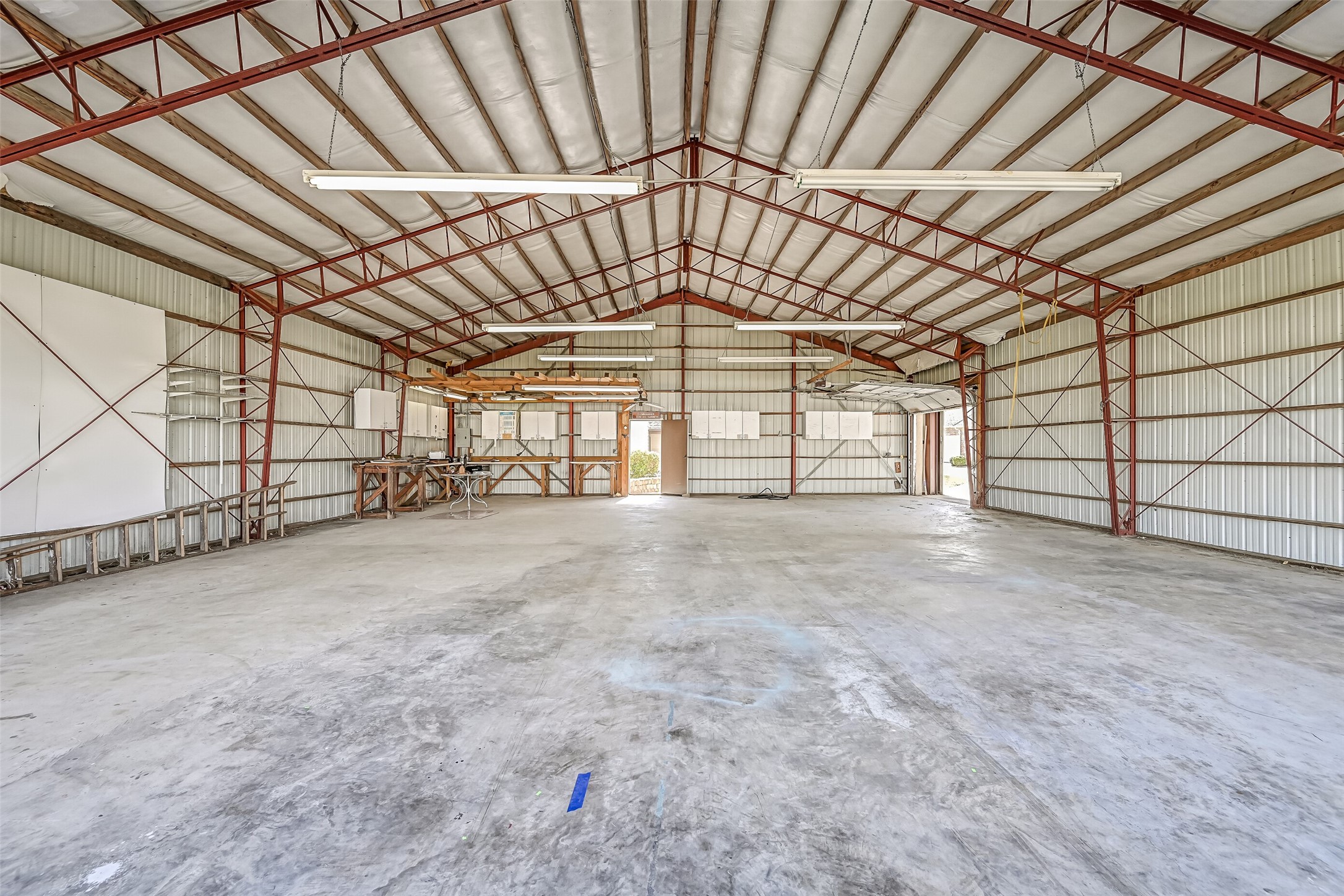 A rare find in Friendswood! This private 48' x 43' airplane hangar features a soaring peaked roof, expansive concrete flooring, exposed structural framing, overhead lighting, and built-in workbenches with storage cabinetry. An exceptional space for aviation enthusiasts with direct access to the community airstrip.