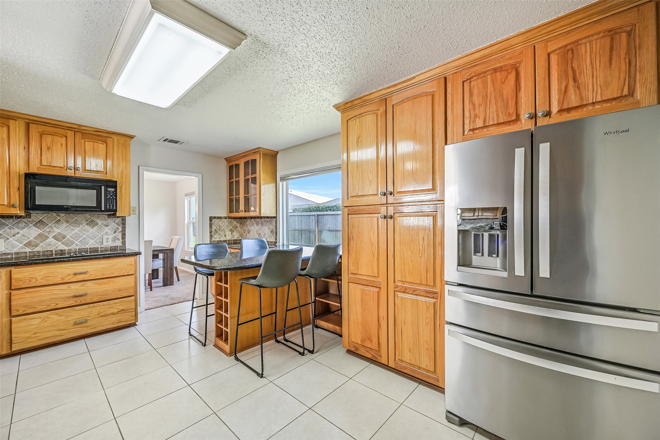 The spacious kitchen offers abundant natural wood cabinetry, granite countertops, decorative tile backsplash & a breakfast bar with seating. A stainless steel refrigerator, built-in appliances & generous storage make this a functional space, with convenient access to the formal dining room.