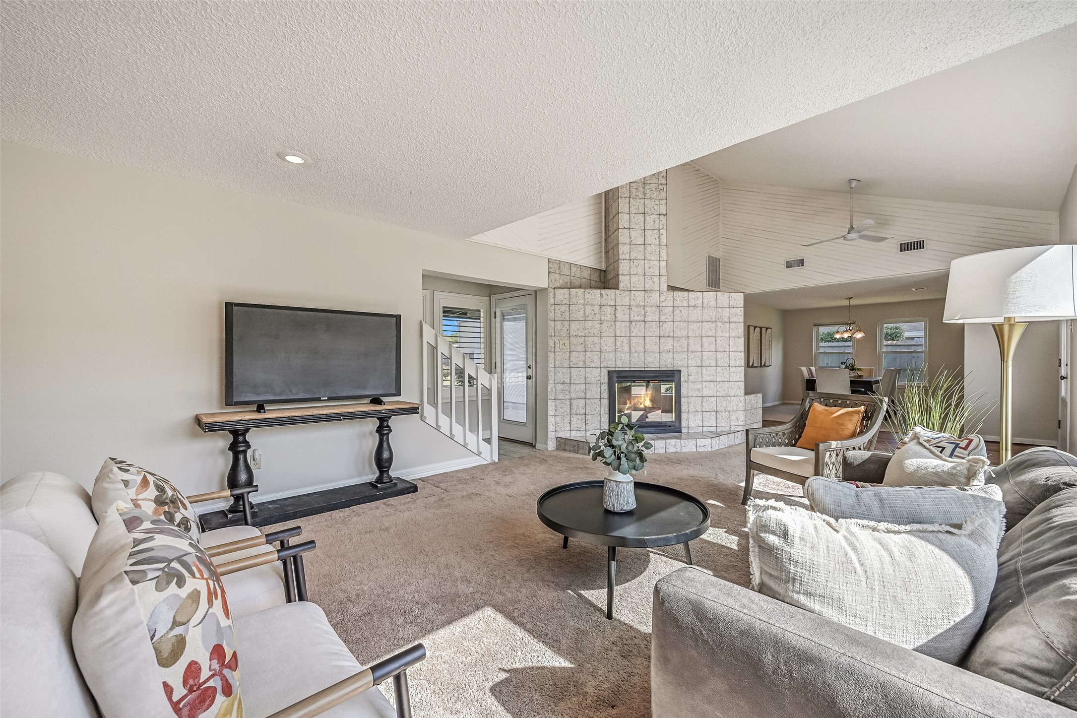 Looking across the spacious living room, the distinctive tiled wood-burning fireplace creates a focal point between the living & dining areas. Soaring ceilings, architectural accents & an open layout provide a sense of spaciousness, with the formal dining room conveniently nearby.