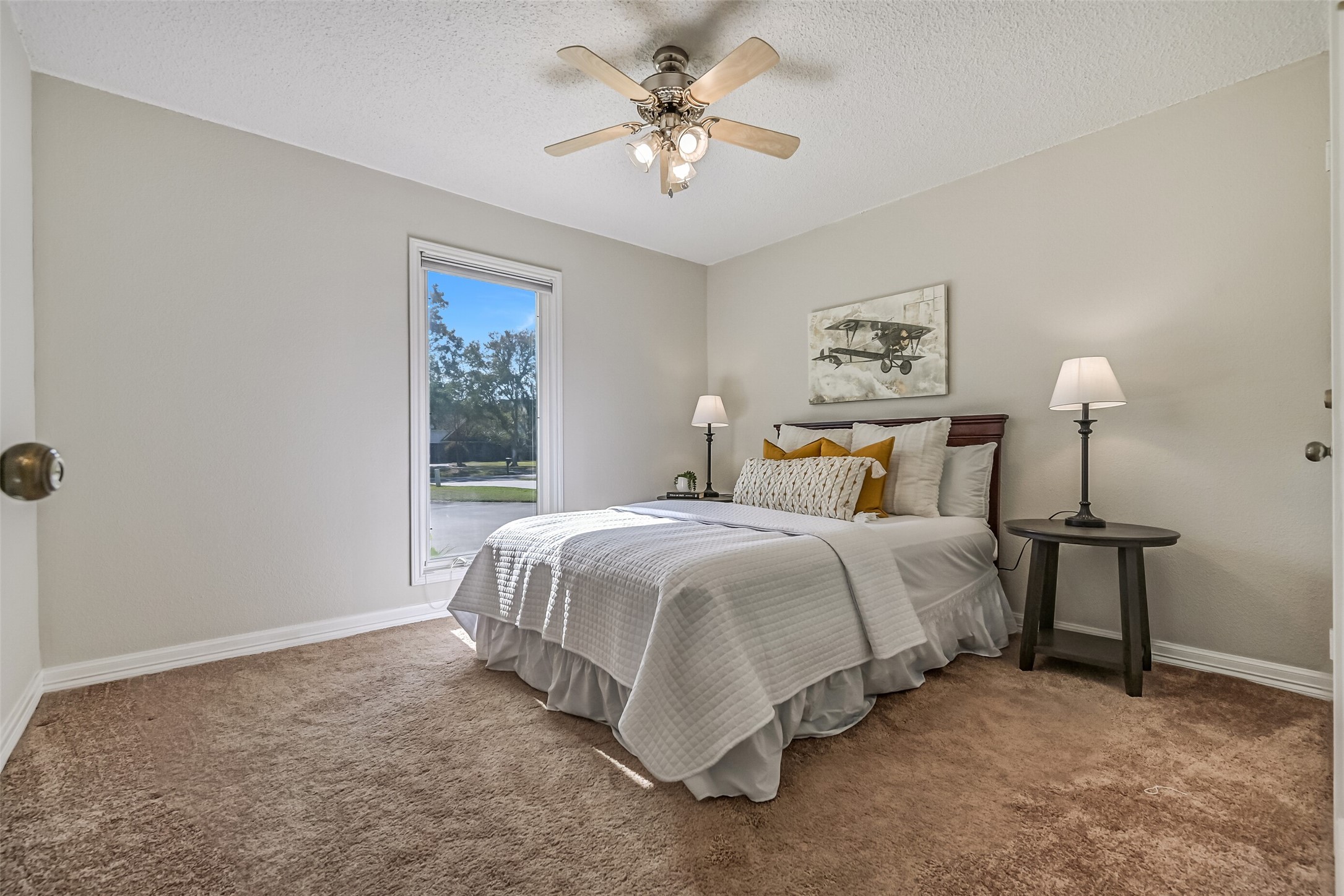 This first-floor secondary bedroom offers neutral carpeting, soft wall colors & a ceiling fan with lighting. A tall window brings in natural light and offers views toward the front of the property. The comfortable layout provides room for bedroom furnishings, with convenient access to the nearby bathroom.