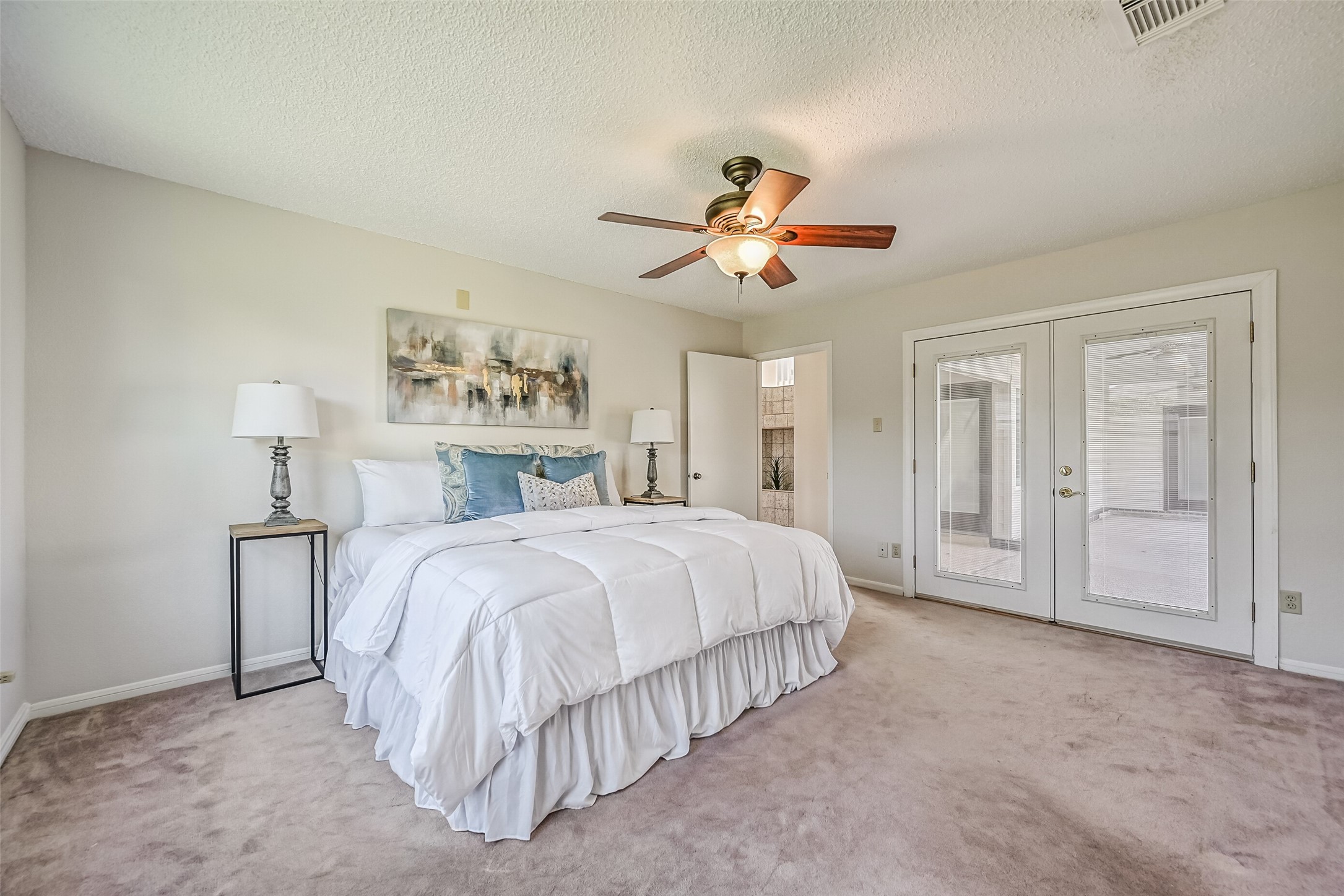 The spacious first-floor primary bedroom offers a comfortable retreat with neutral carpeting, soft wall colors & a ceiling fan. French doors open directly to the covered backyard patio, providing convenient access to the swimming pool and outdoor living area just steps away.